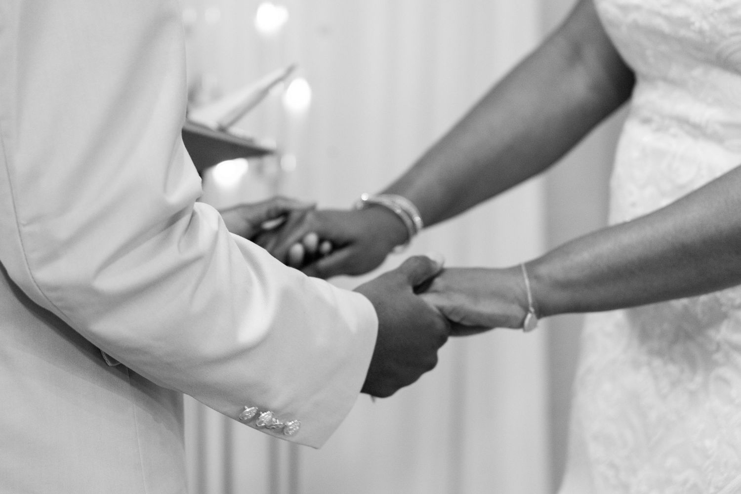 A couple holds hands during a wedding ceremony in a black and white photo.