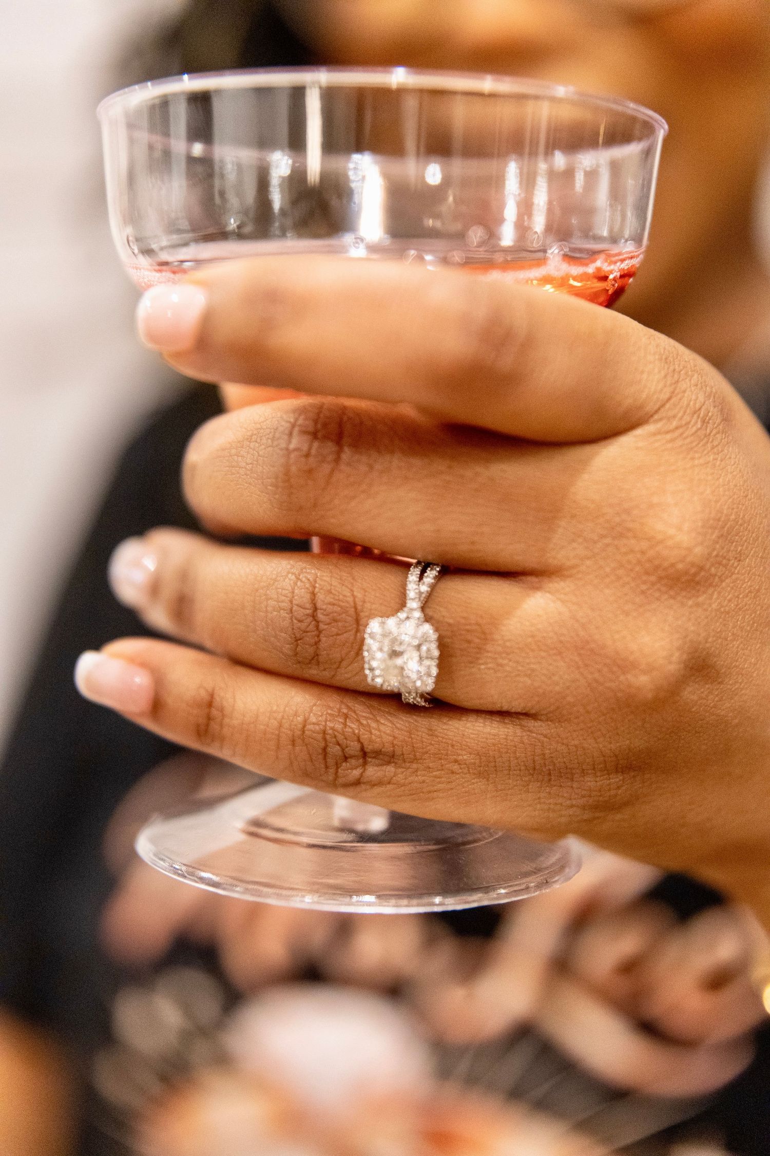 Close-up of hand wearing diamond engagement ring while holding a glass of rose-colored drink. Bridal shower