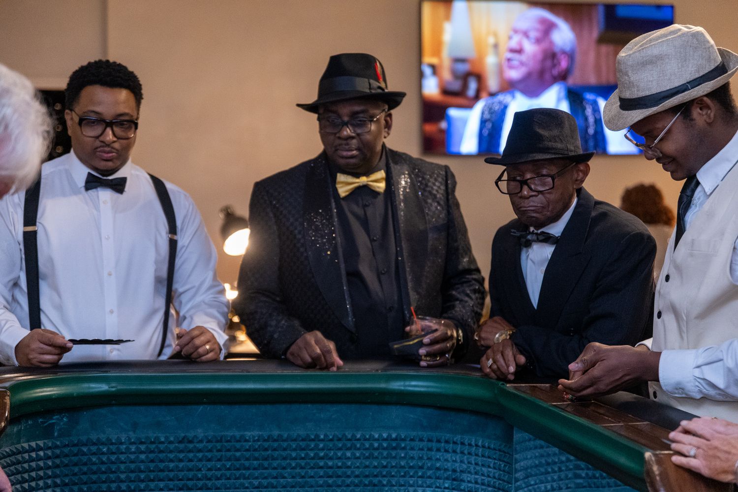 Group of men in formal attire gathered around a green casino table.