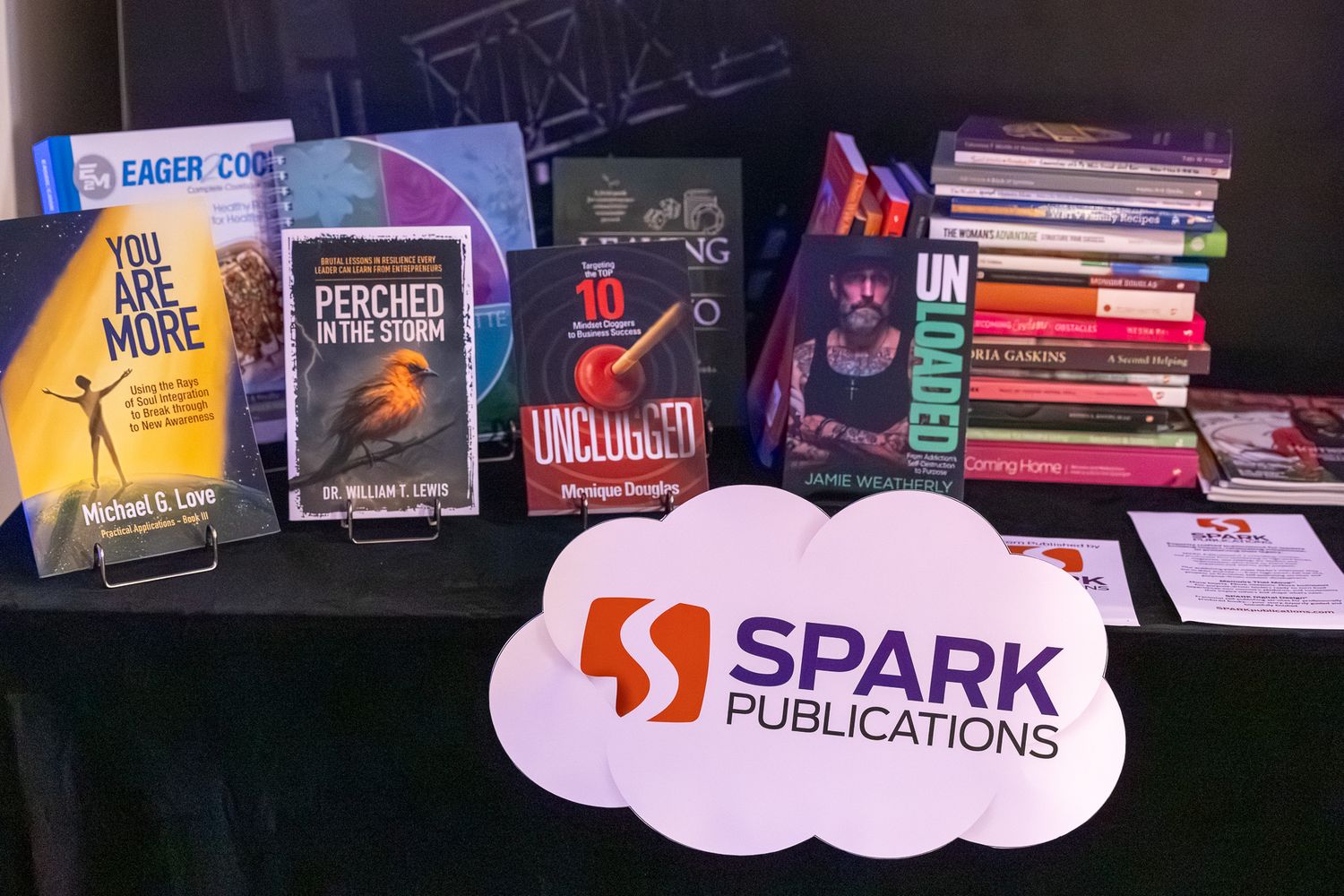 Spark Publications book display featuring titles like You Are More and Perched in the Storm on a table with a branded logo sign.