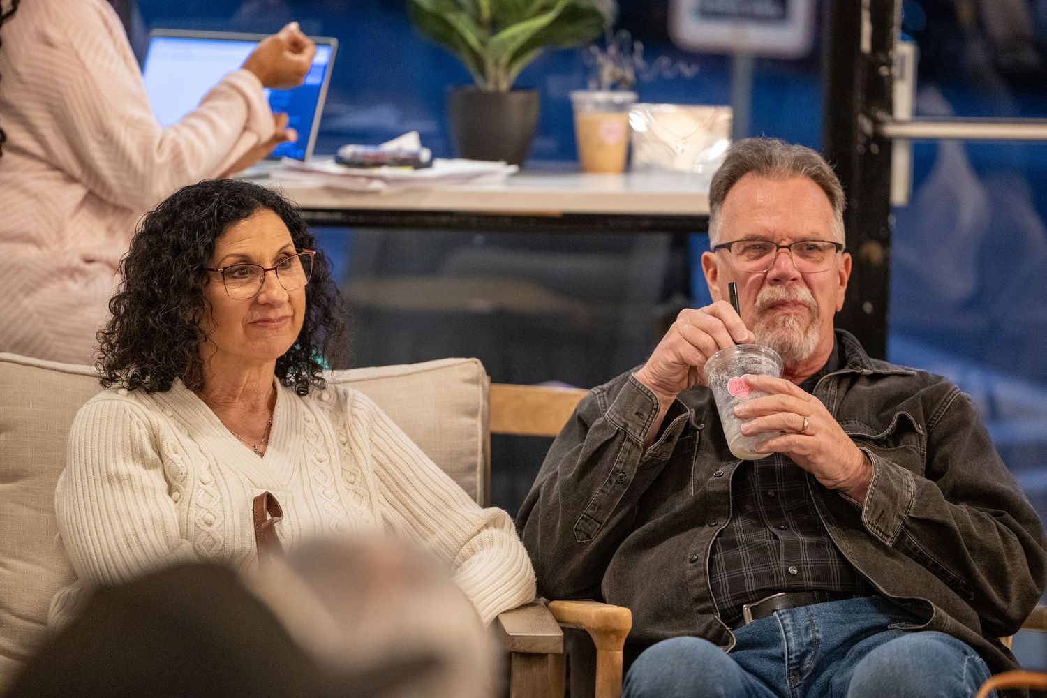 Mature couple relaxing on couch at a casual indoor gathering, man holding a drink.