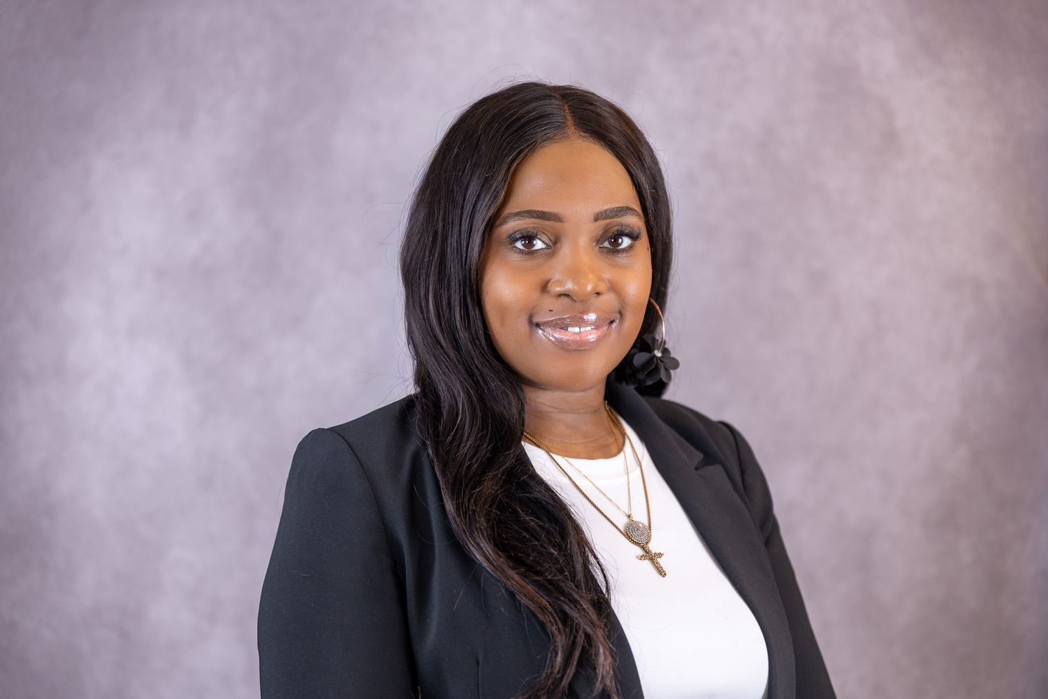 A professional Black woman in a black blazer and white top smiles in a formal headshot portrait.