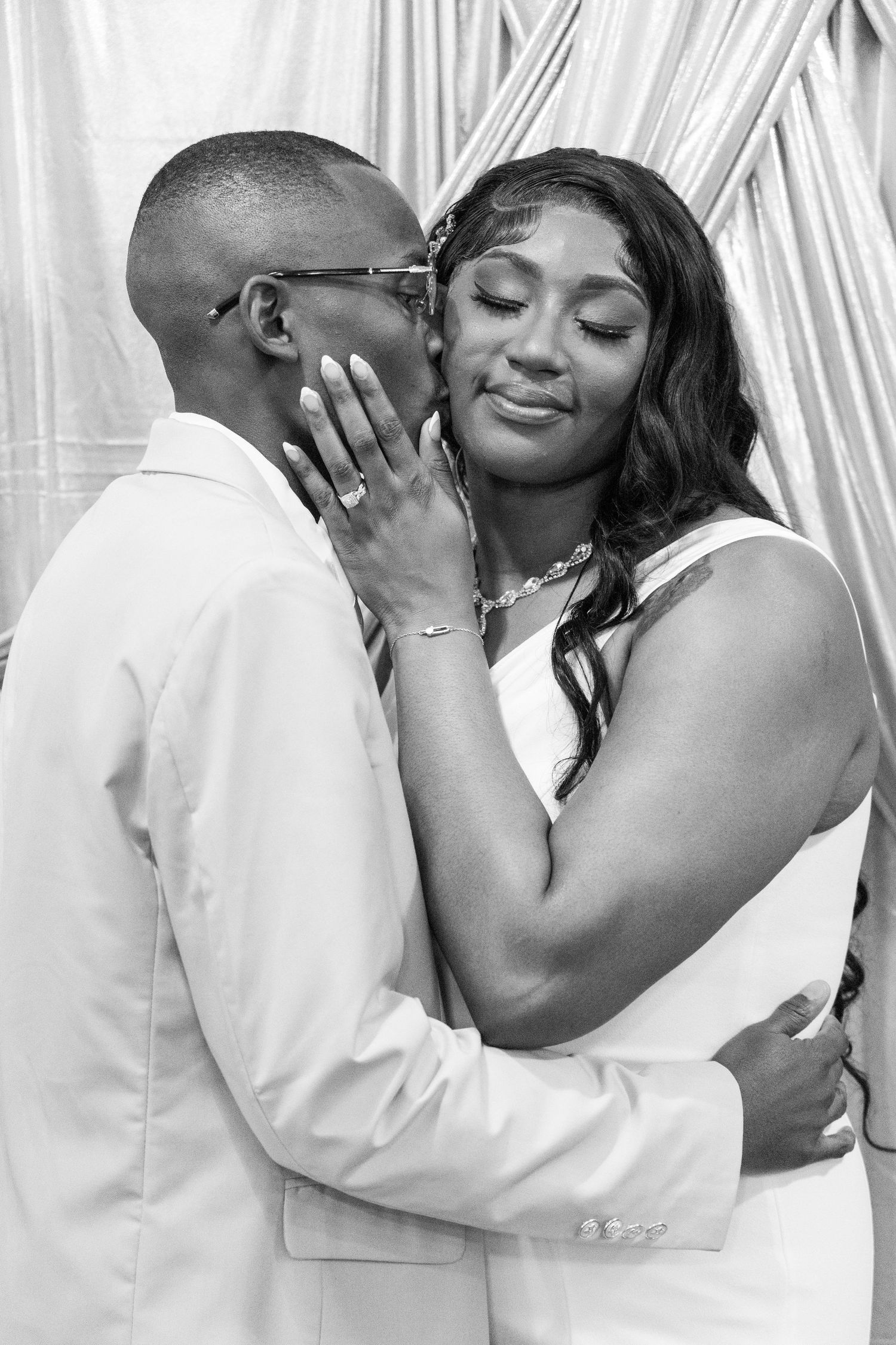 Black and white photo of groom whispering to smiling bride during intimate wedding moment.