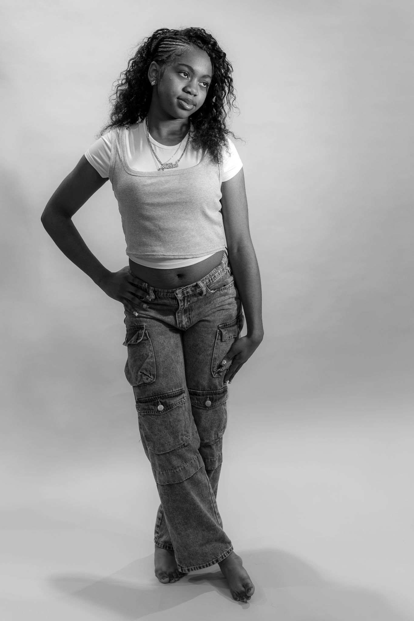A young Black woman poses confidently in a white crop top and cargo jeans in a black and white studio photo.