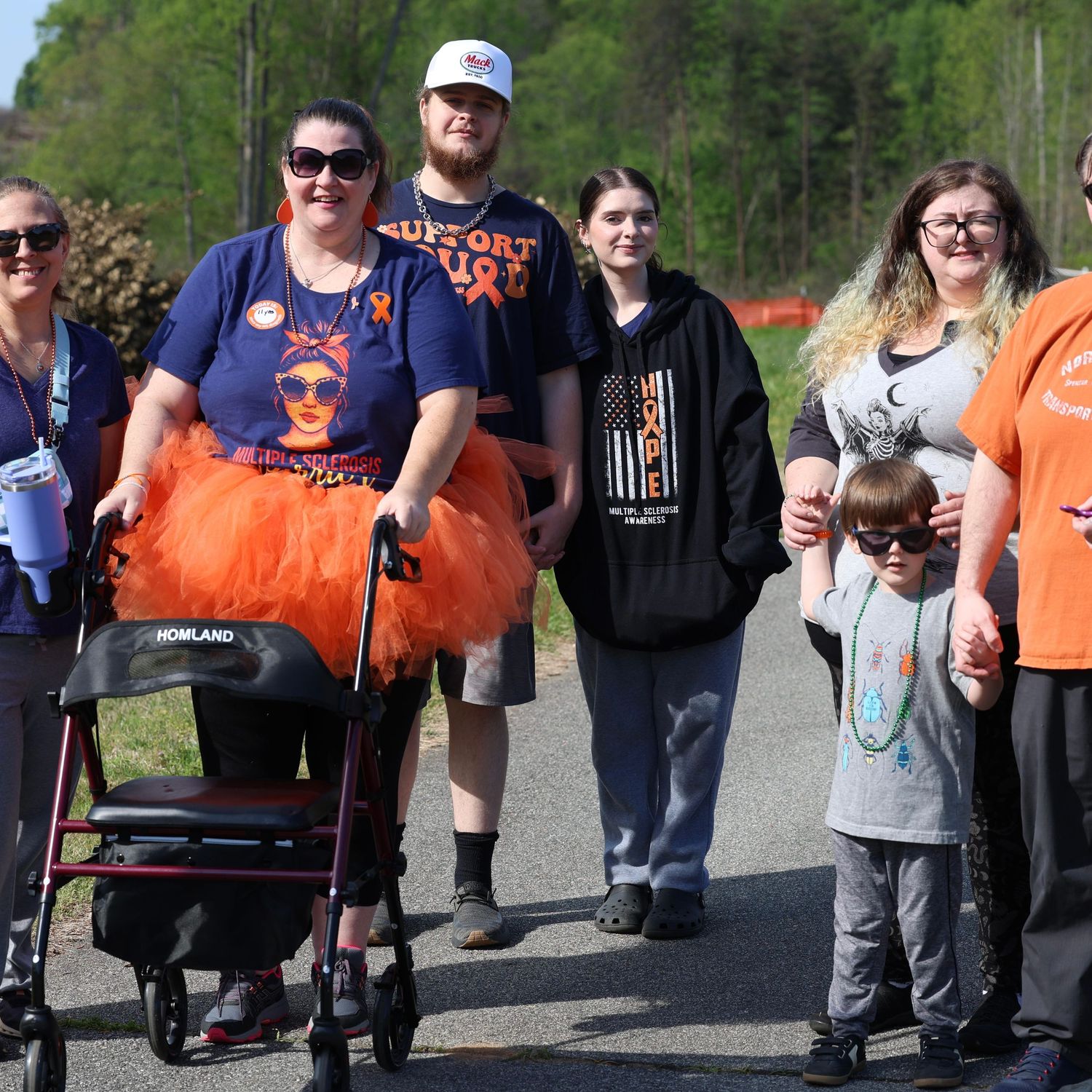 Group of people wearing orange outfits walking together at a charity awareness walk event outdoors. Multiple Sclerosis. Walk MS