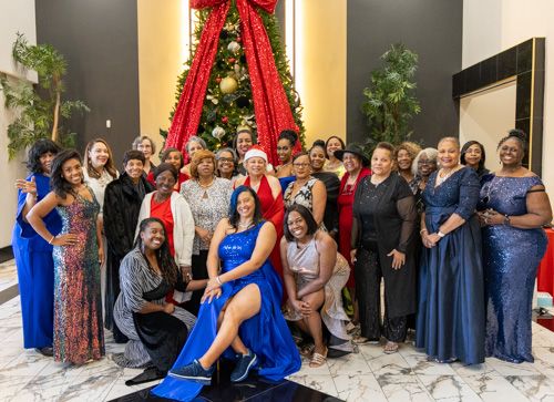 Large group of elegantly dressed people posing together near a decorated Christmas tree indoors.