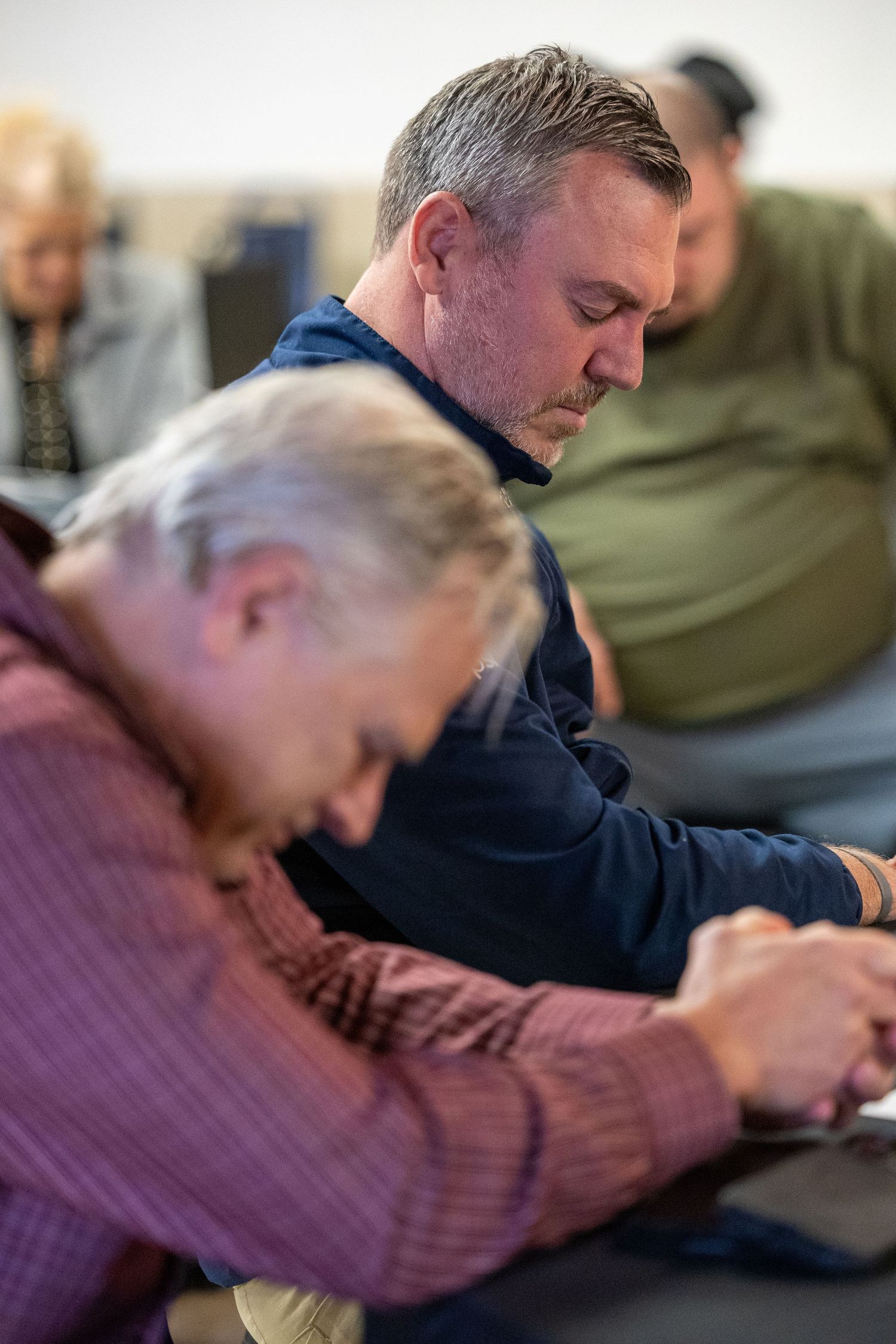 Group of adults bowing heads in prayer during a church service or religious gathering.