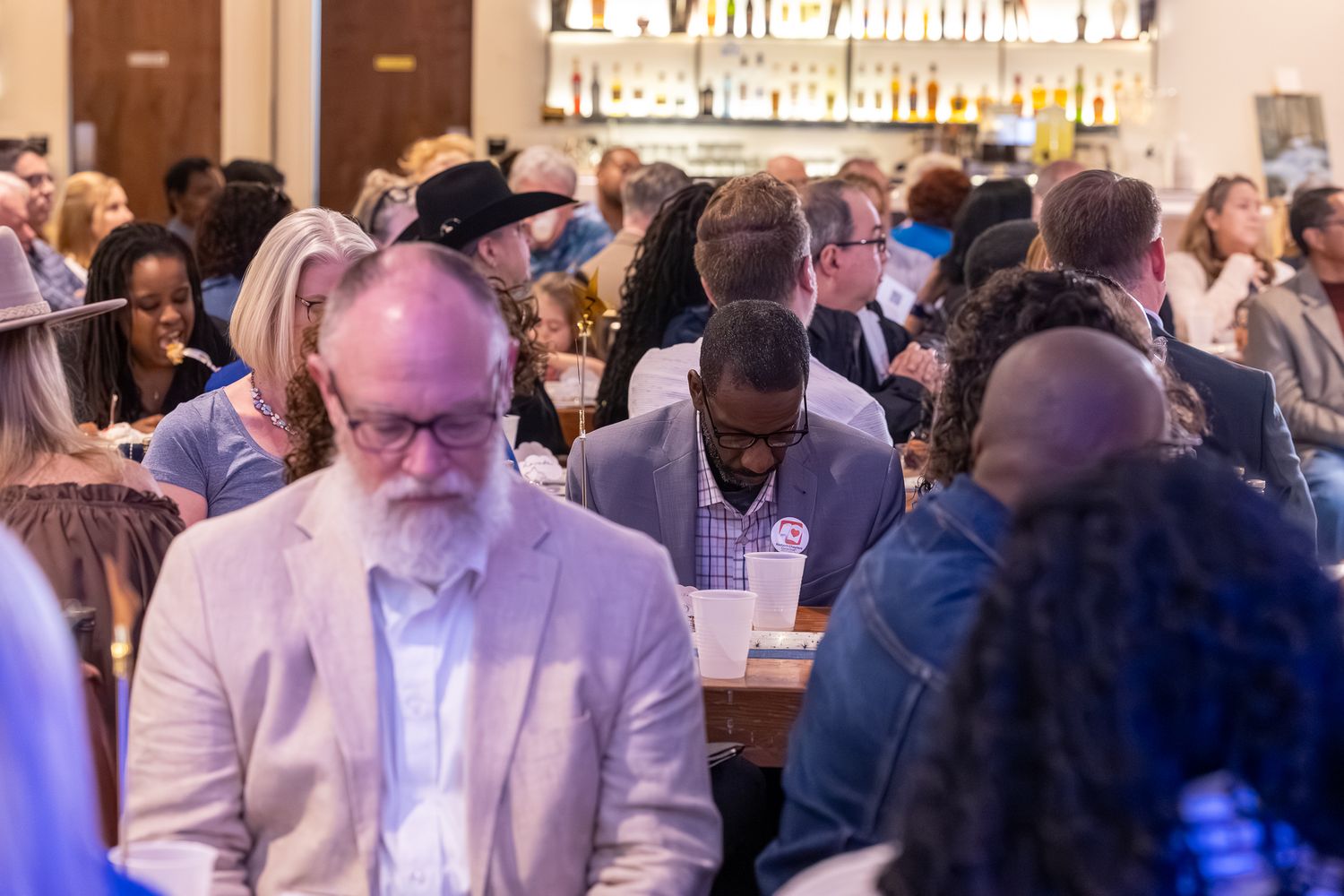 Diverse crowd of professionals networking at a busy indoor event with drinks and conversation.