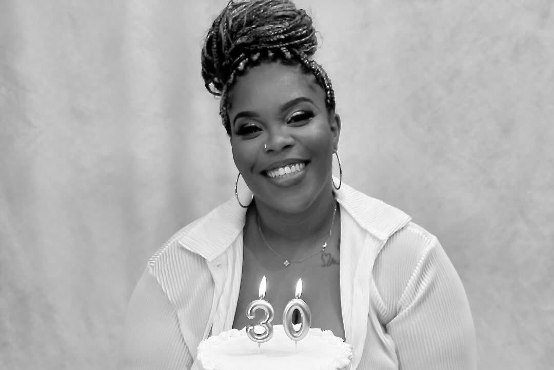 Woman smiling and holding 30th birthday cake with candles in black and white celebration portrait.