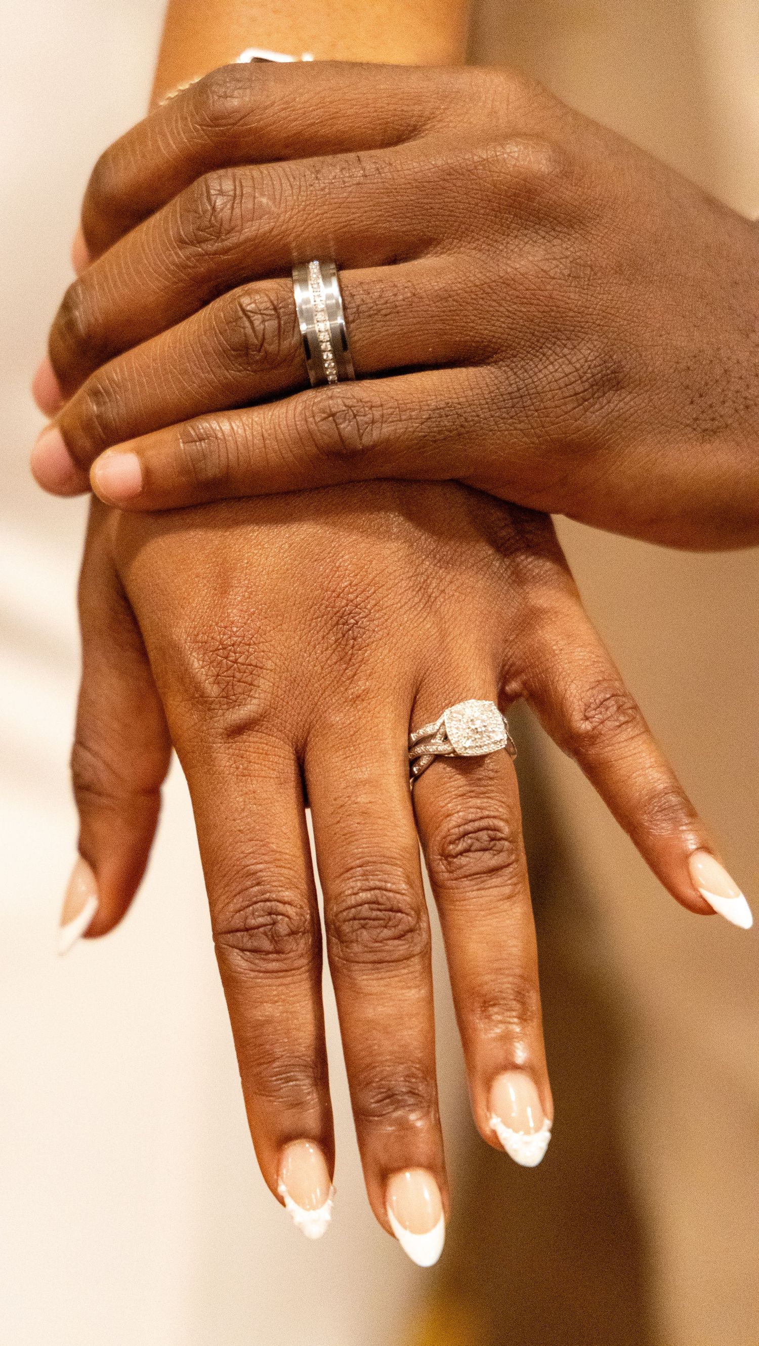 Close-up of newlyweds hands displaying sparkling diamond engagement ring and wedding bands.