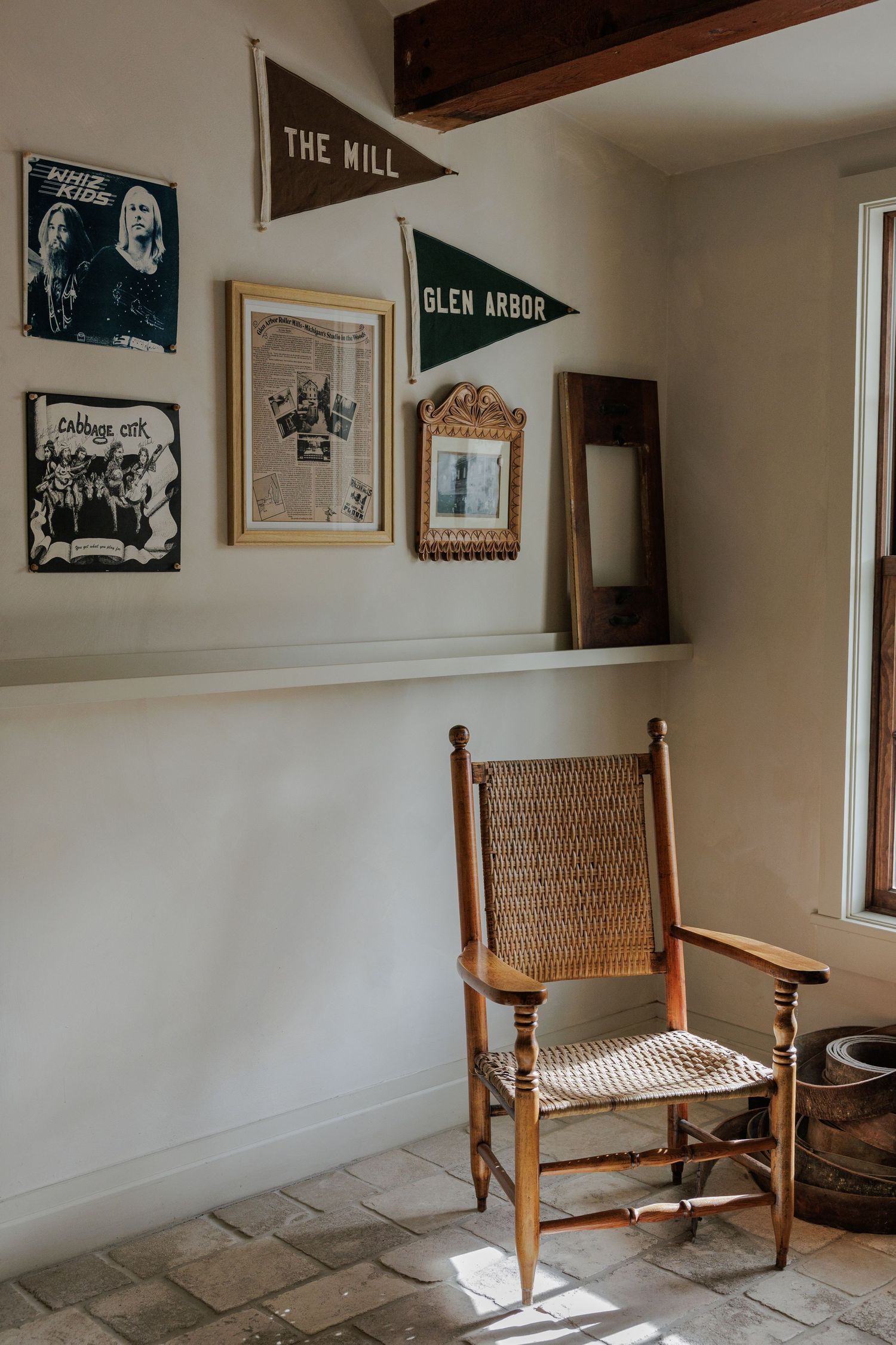 Rustic wooden chair with woven cane seat sits against white wall decorated with vintage black and white photographs.