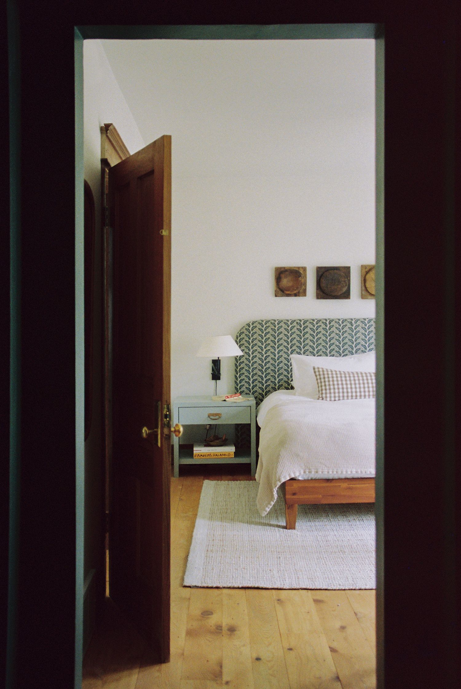 Modern bedroom interior with wooden floors and geometric patterned headboard against white walls.