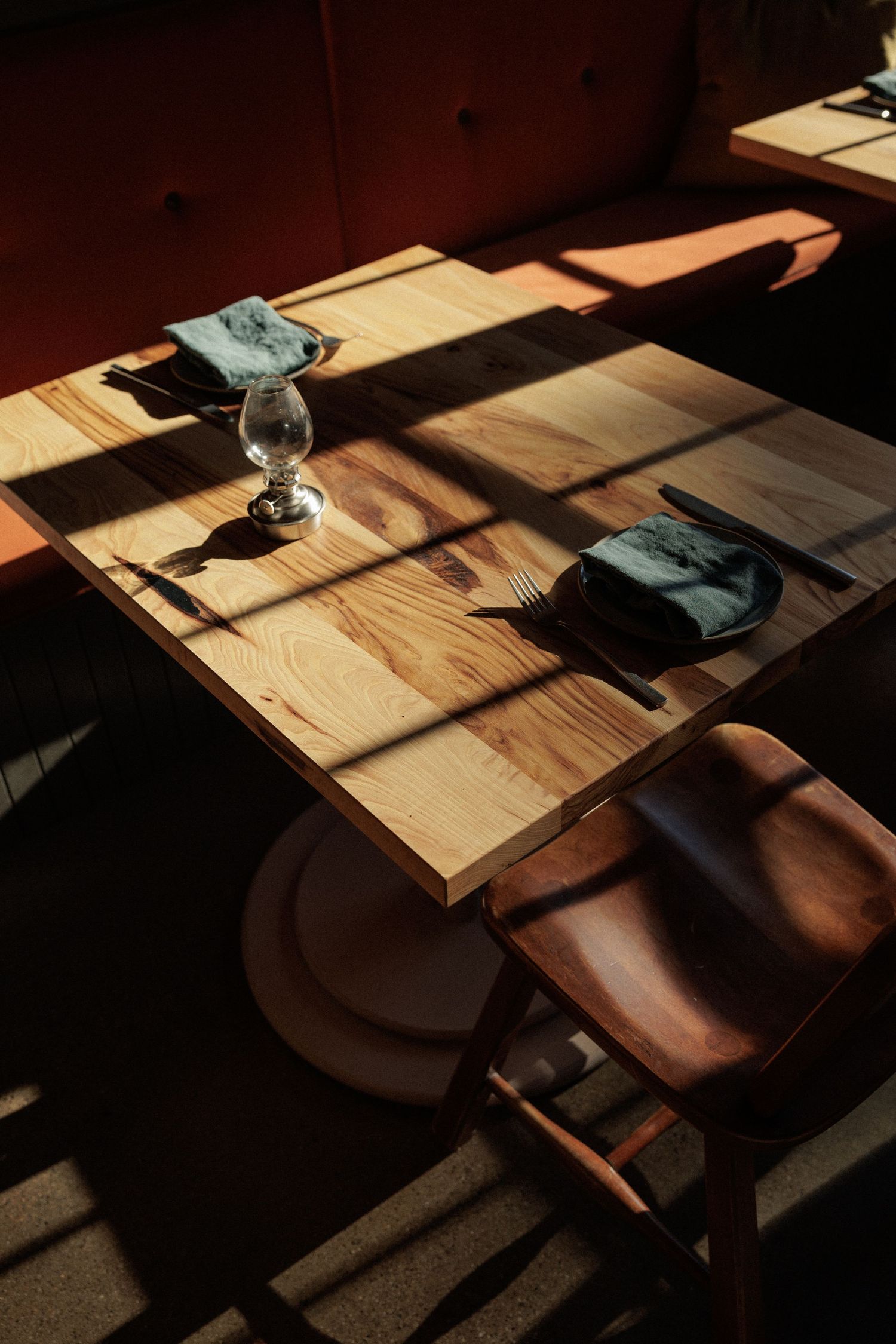 Wooden dining table setting with dramatic shadows and natural light streaming through windows.