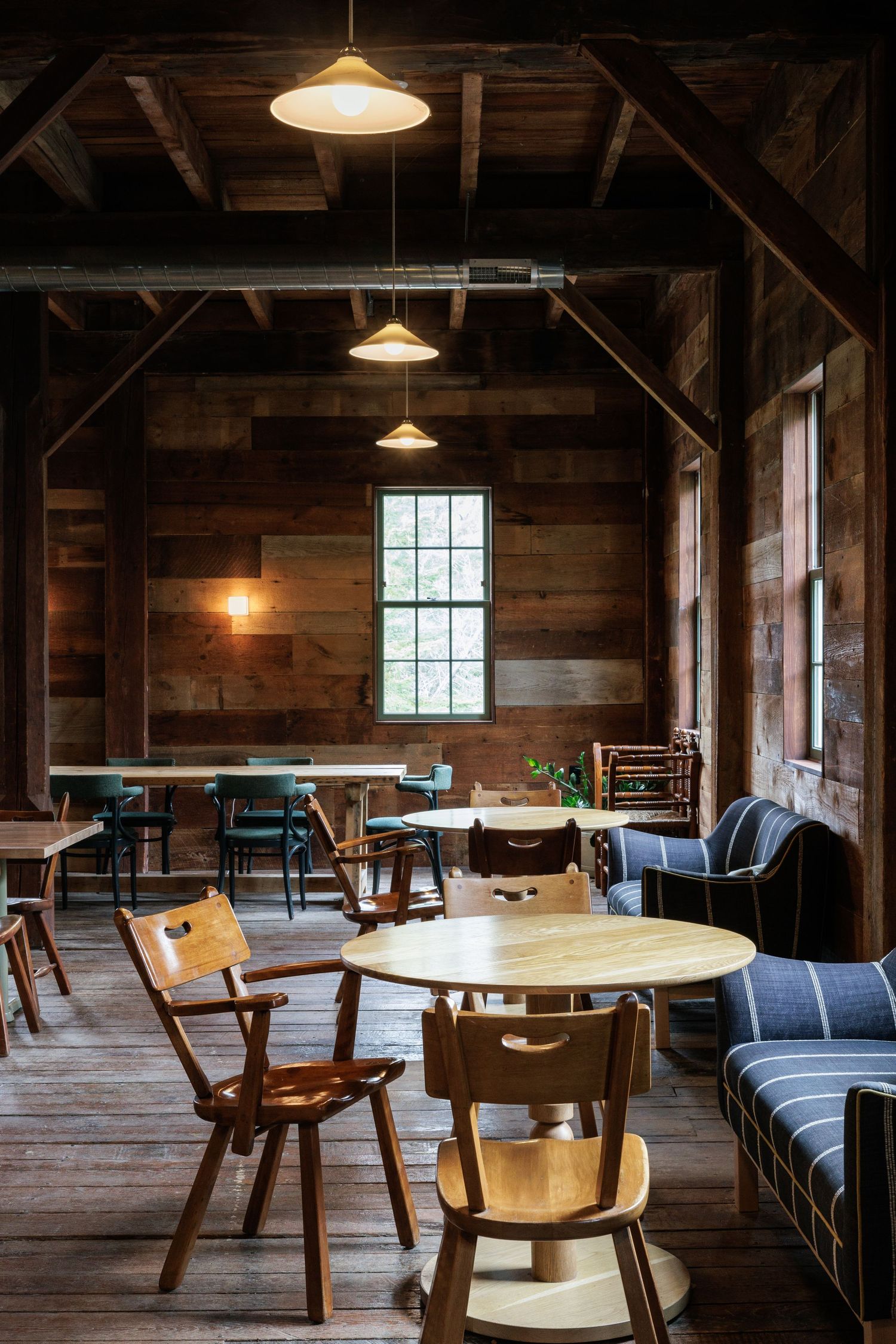 Rustic cafe interior with wooden walls, pendant lights, and mixed vintage furniture.