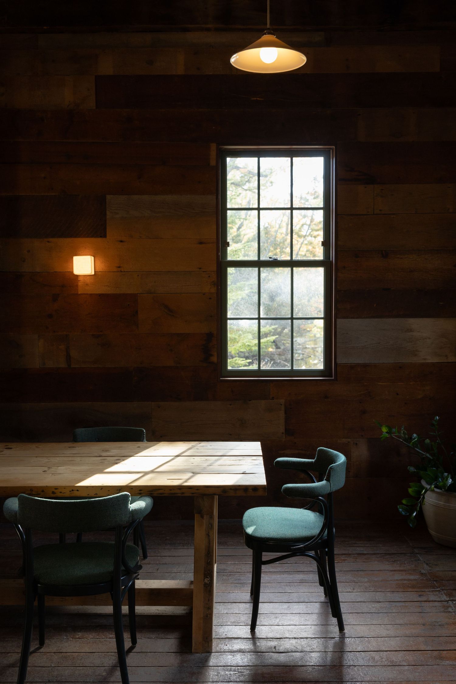 Dark rustic interior with wooden tables and chairs illuminated by natural window light.