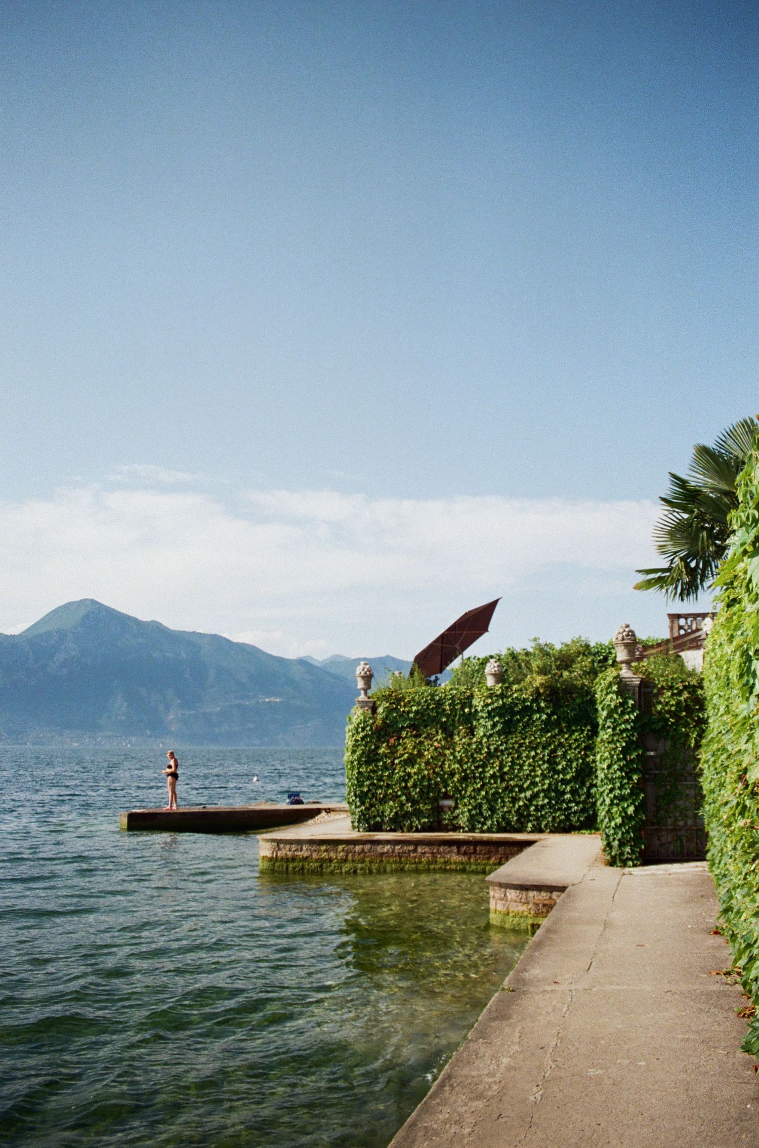 Lakeside walkway with mountains and palm trees along the waterfront.