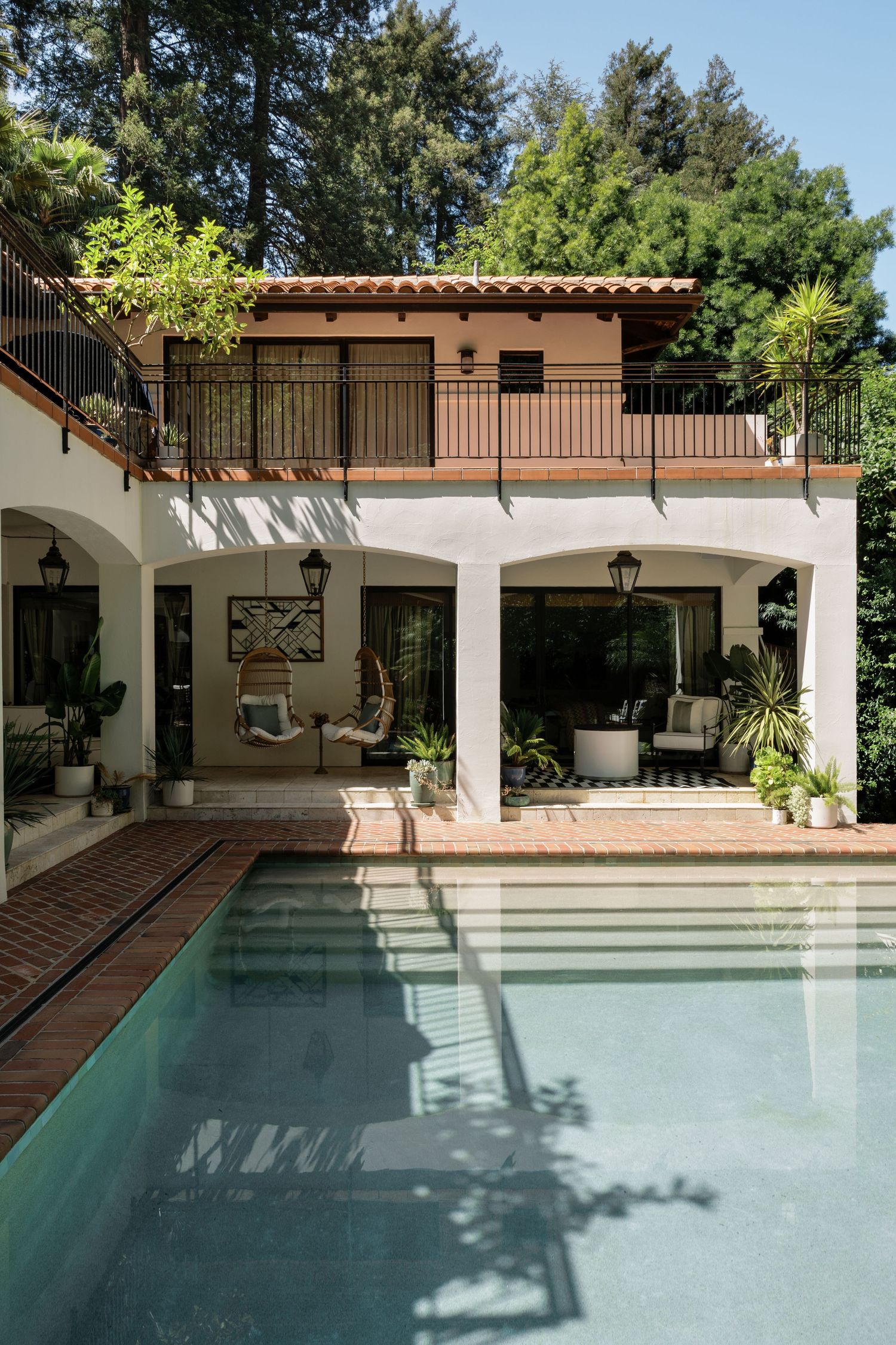 Luxurious outdoor pool area with white columns, covered patio, and surrounding landscaping.