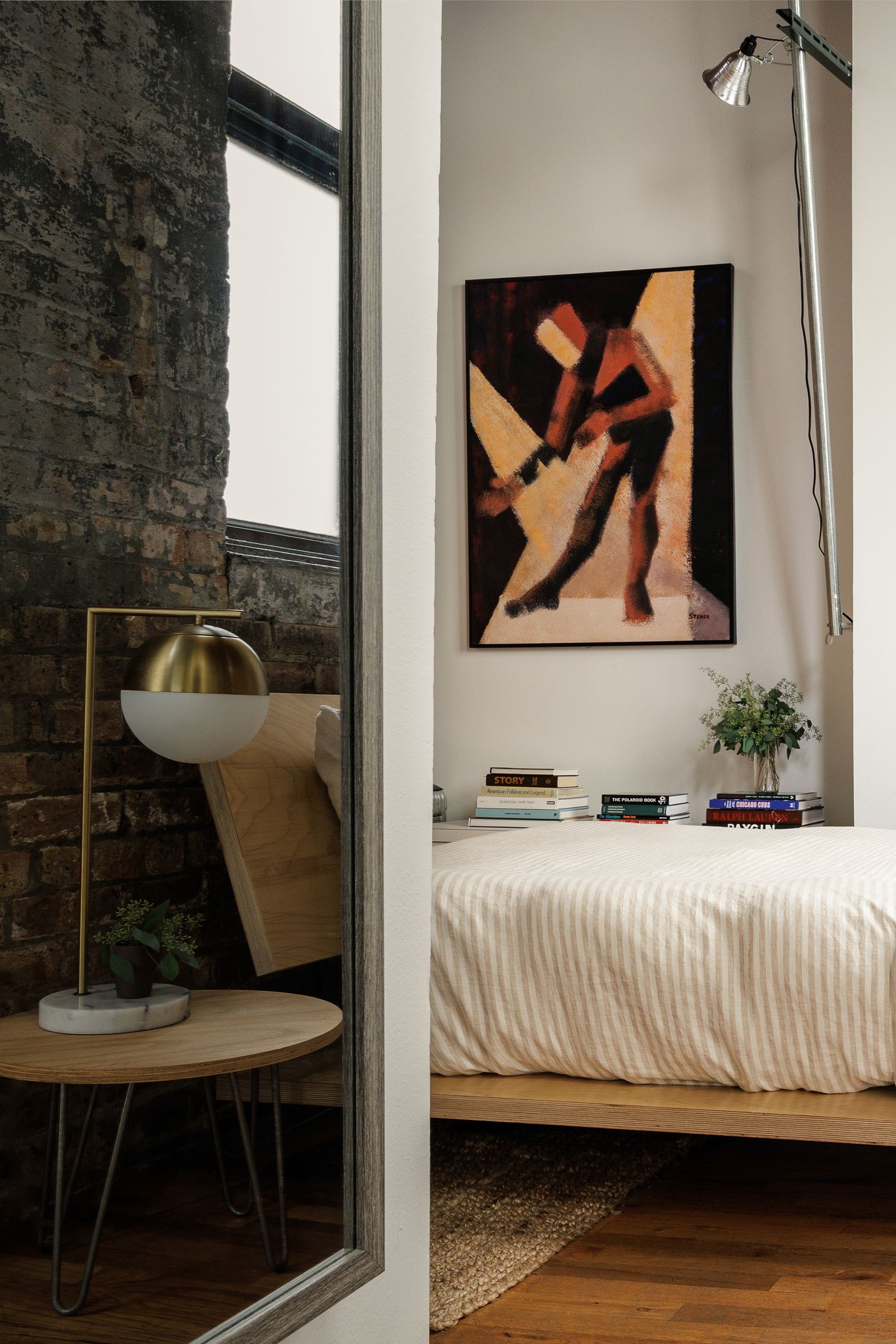 Modern bedroom interior with exposed brick wall, hardwood floors, and abstract wall art in warm earth tones.