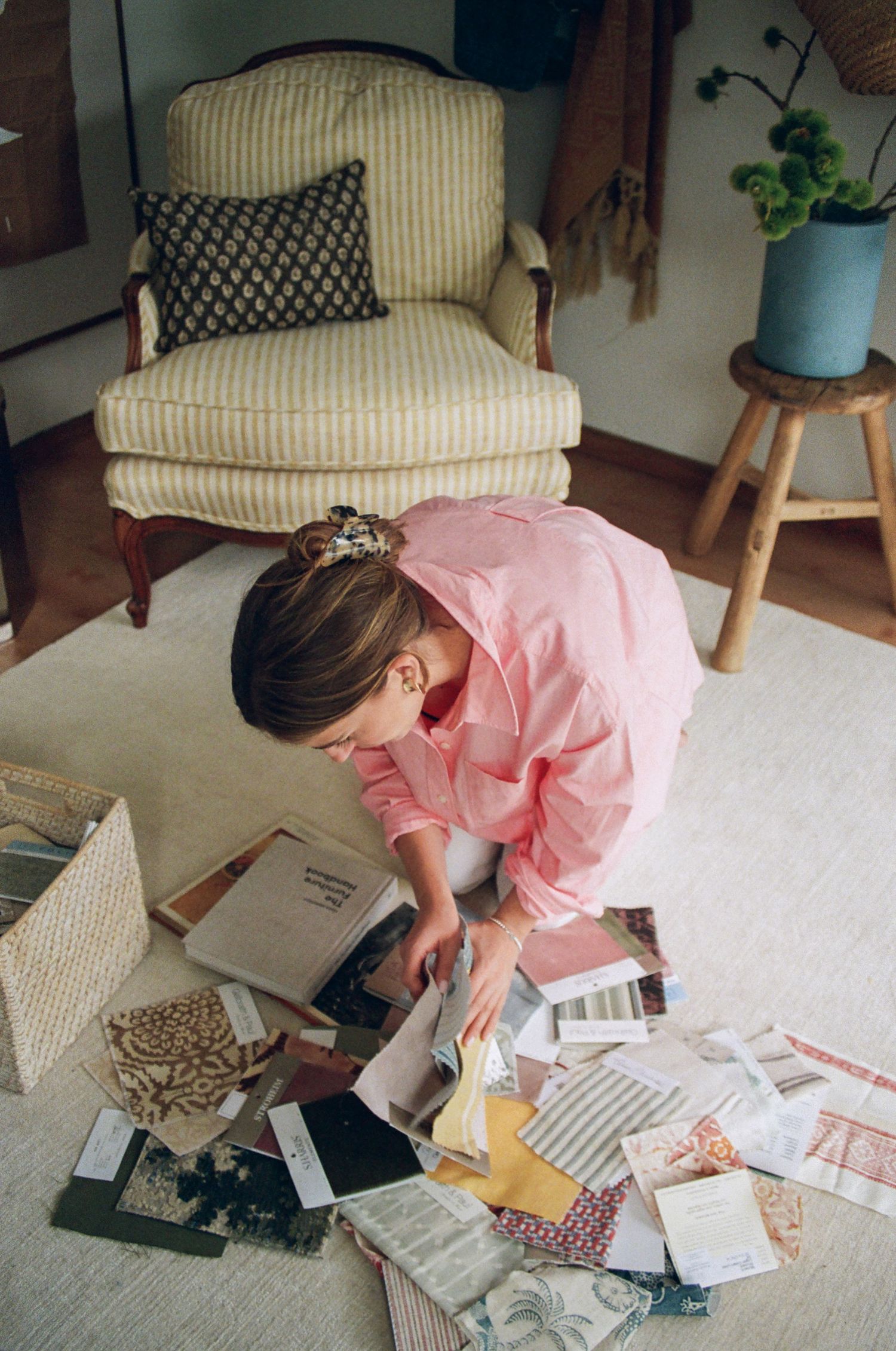 A woman sits on the floor surrounded by various papers and materials, suggesting a creative or work-related activity.