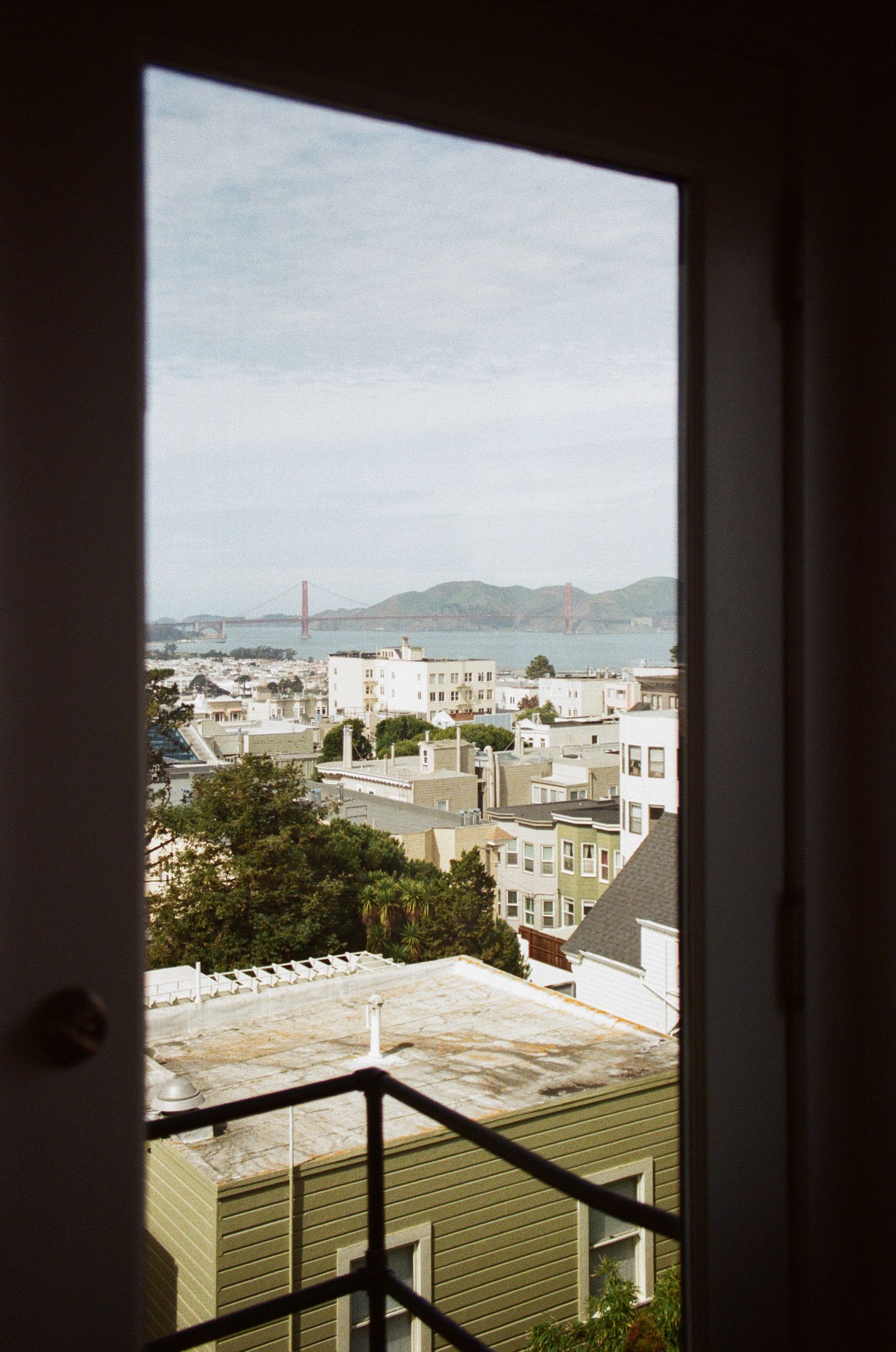 Urban cityscape view through dark window frame showing the Golden Gate Bridge in distance.
