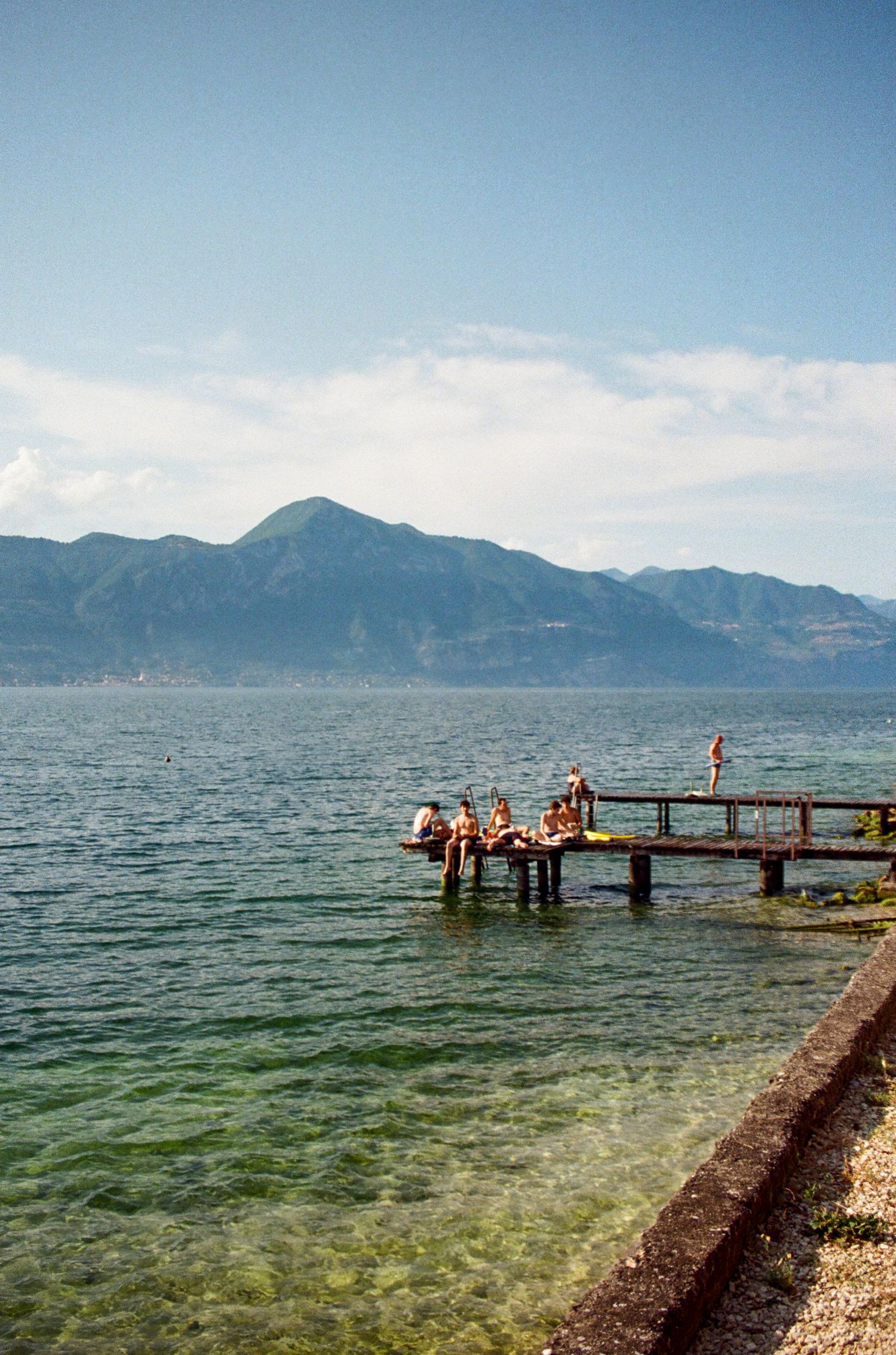 Wooden pier extending into a mountain lake where people are swimming and relaxing.