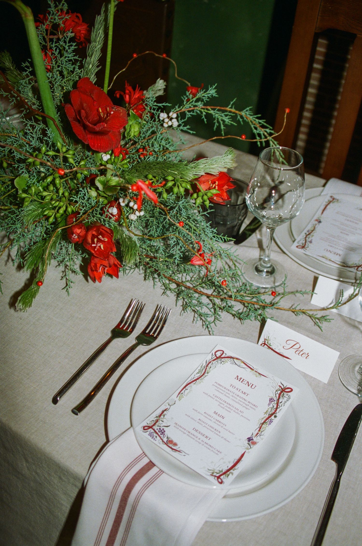 Formal place setting with red floral centerpiece and elegant menu card on white tablecloth.