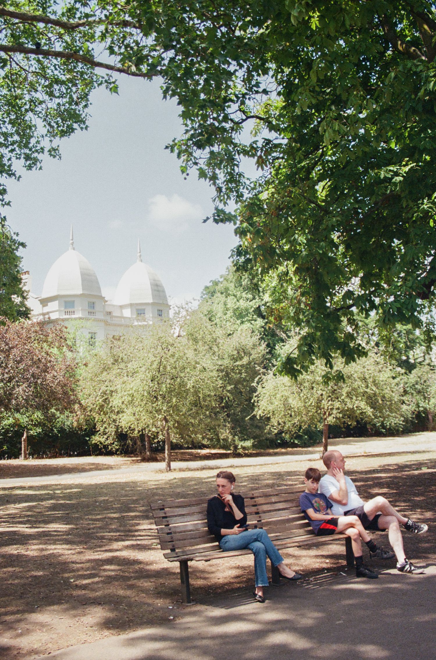 People relaxing on benches in a shaded park area on a sunny day.