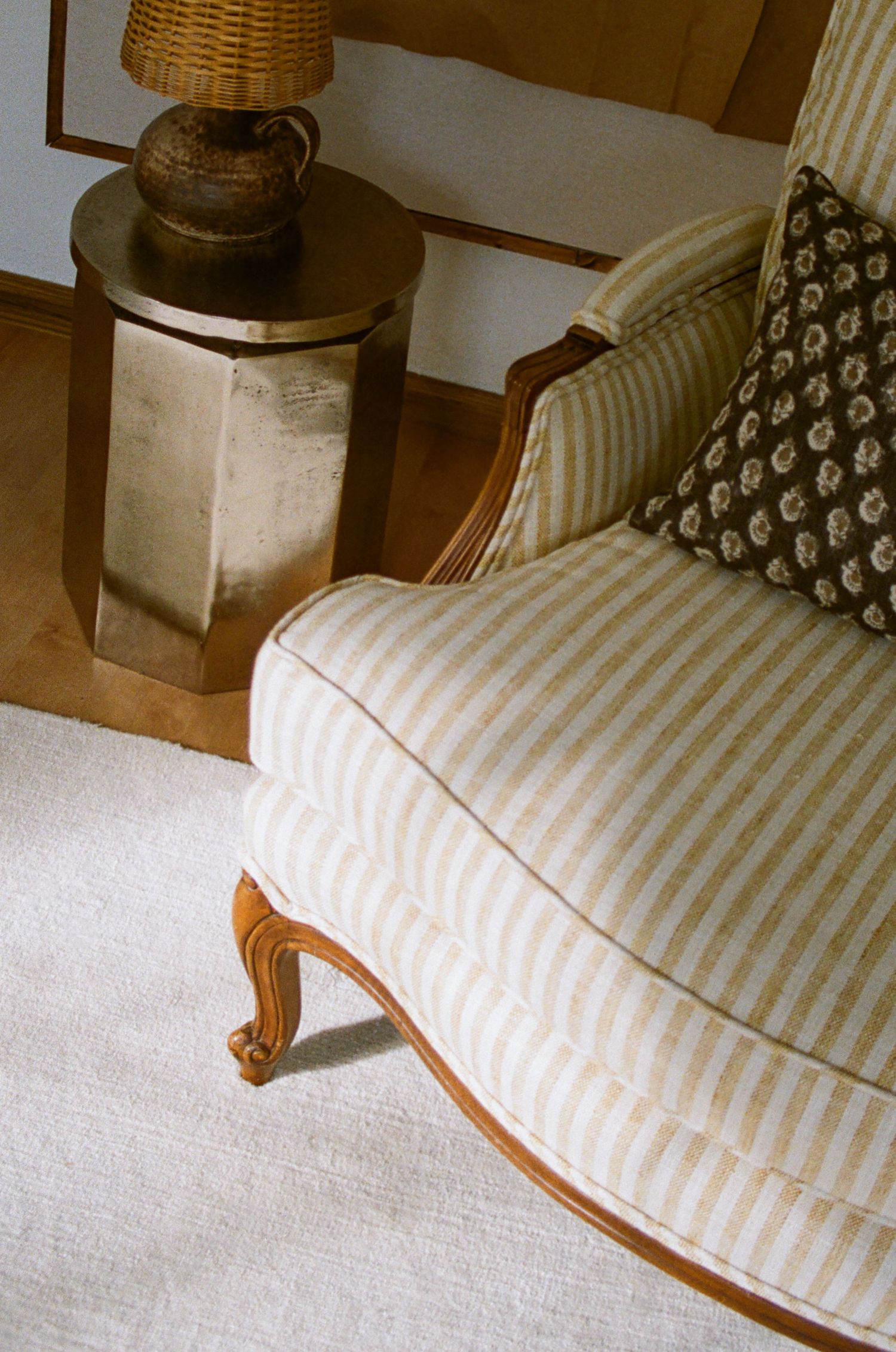 The image shows a cozy living room with a striped upholstered chair, a woven basket lamp, and a decorative vase on a side table.