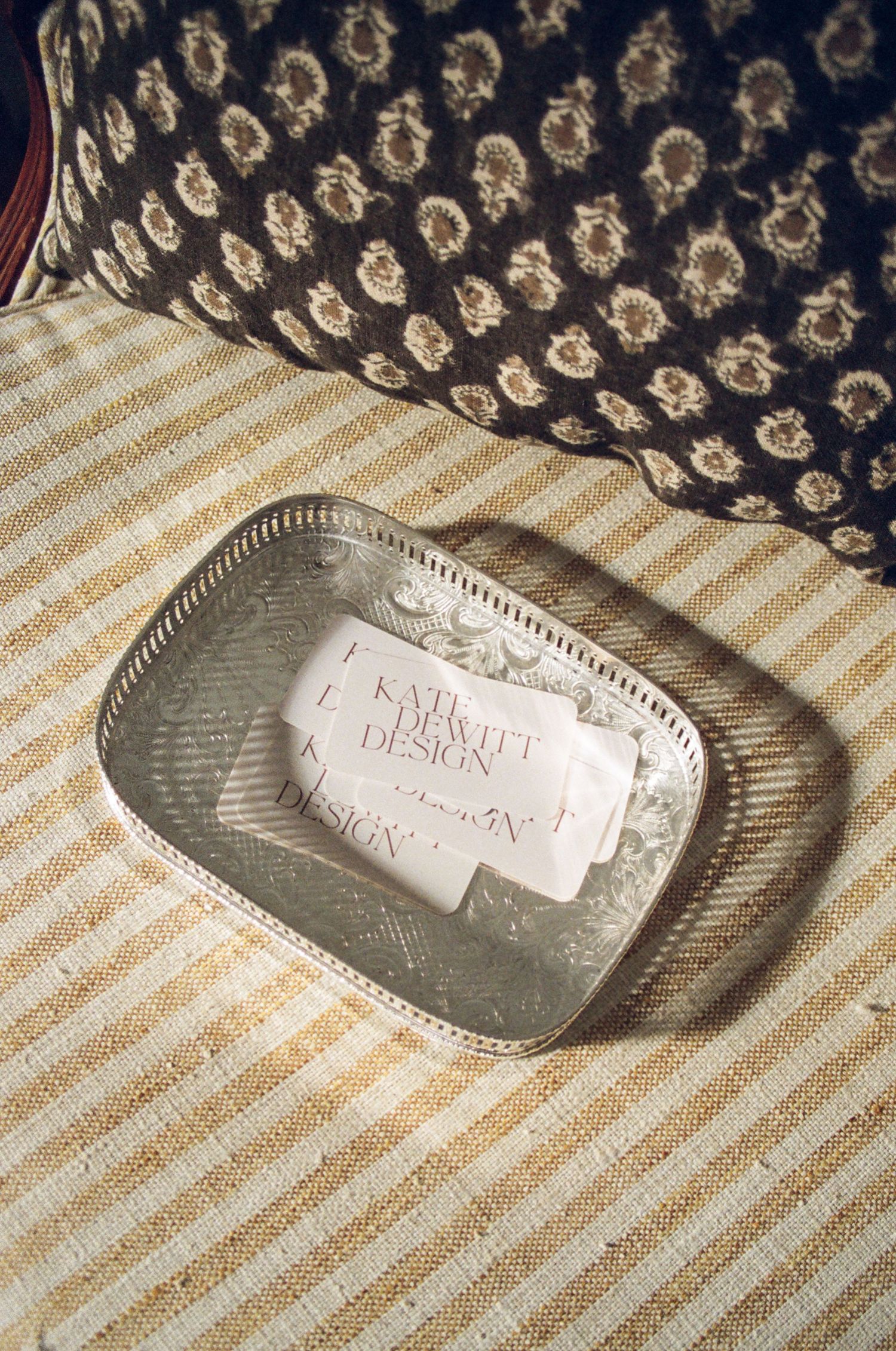 A silver rectangular tin or container rests on a striped fabric background.