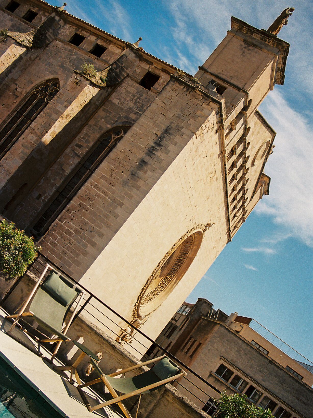 Historic stone church tower with ornate rose window viewed from below against blue sky with outdoor terrace seating.