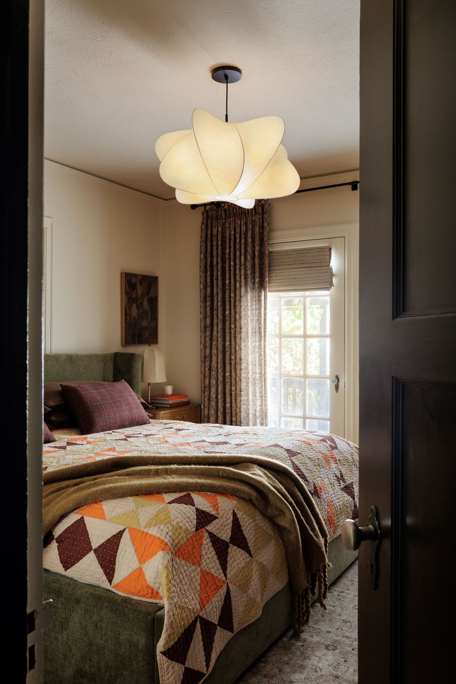 Bedroom interior with orange and gray geometric bedspread and modern lighting.