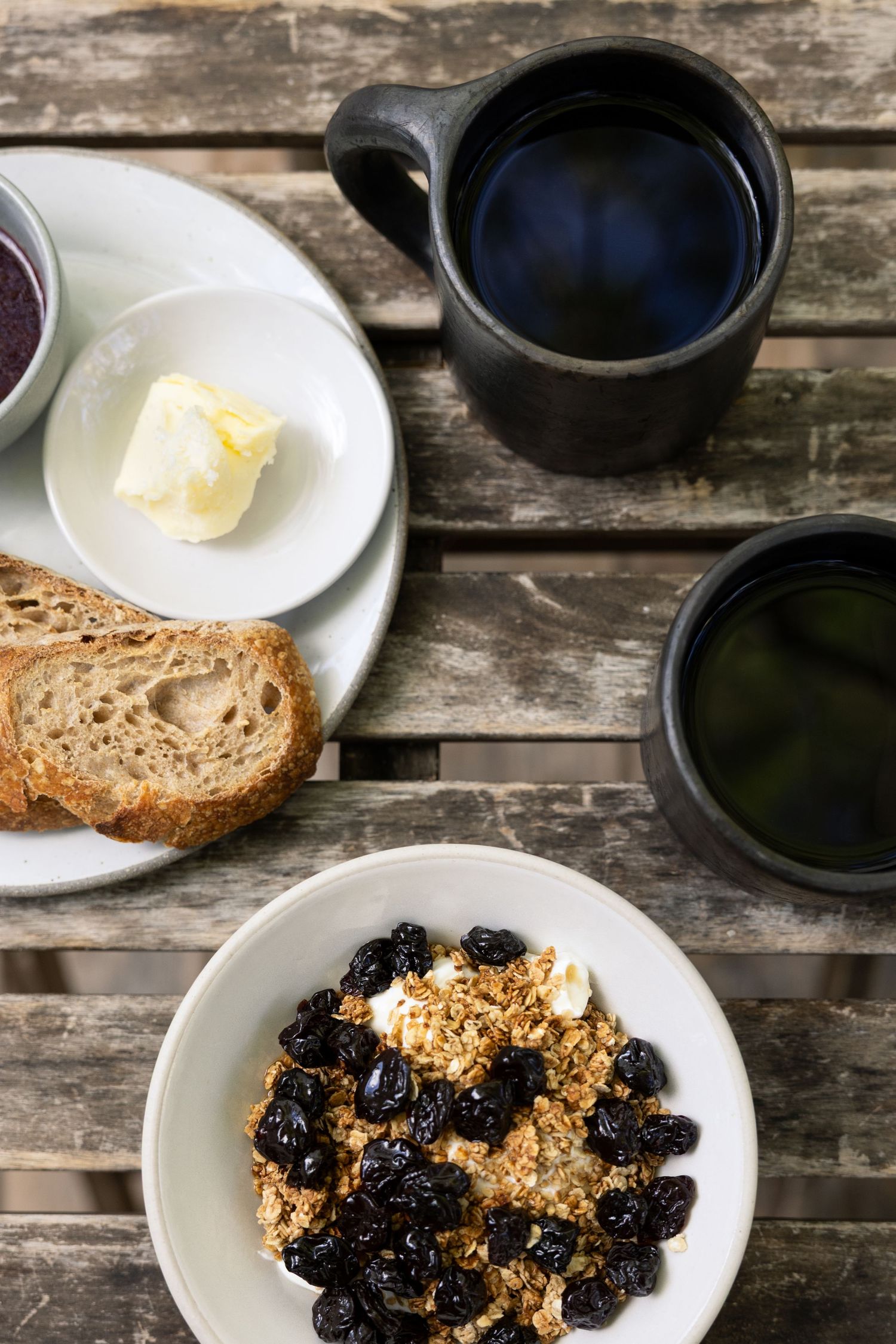 Progression of breakfast items being added to plates on a weathered wooden table surface.
