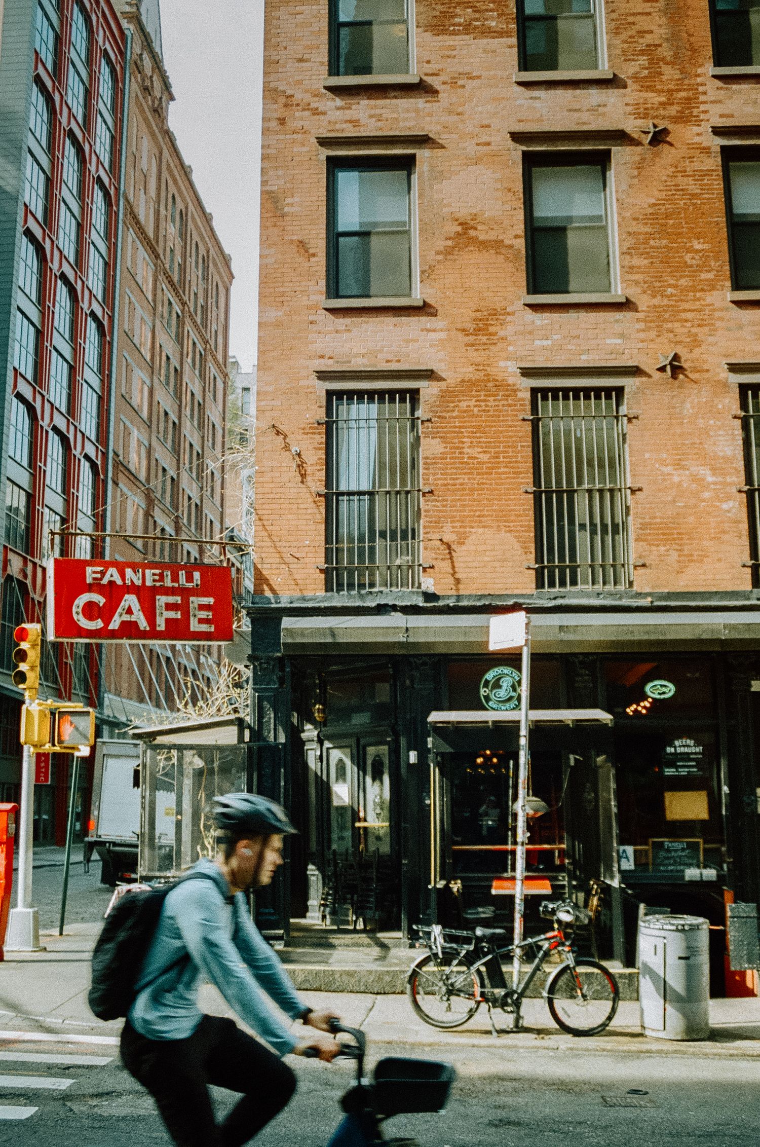 Brick building with Fanelli Cafe sign and cyclists passing by on the street.