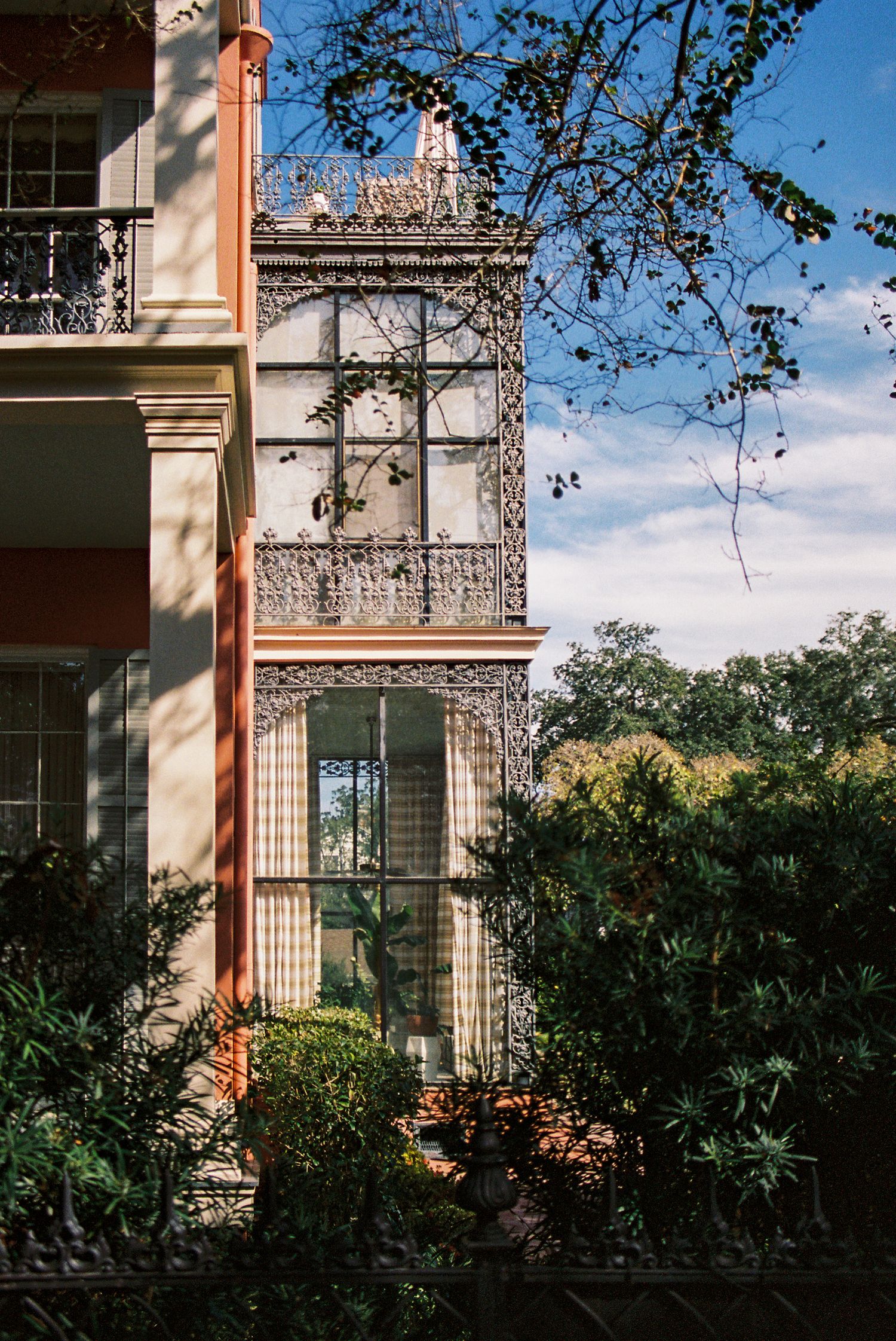 Elegant building exterior with ornate balconies and lush landscaping in sunlight.