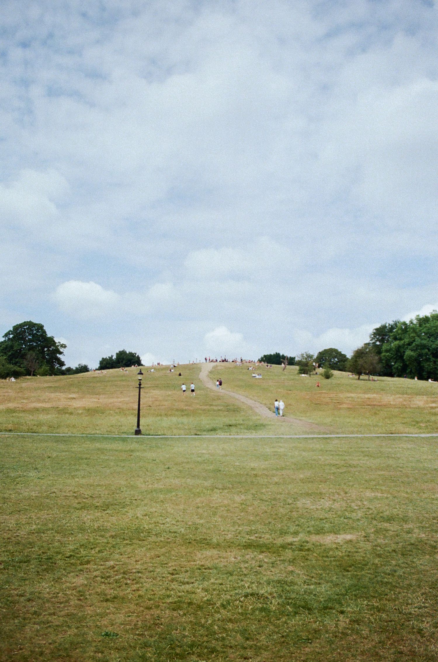Rolling green hillside under cloudy skies with distant figures visible.
