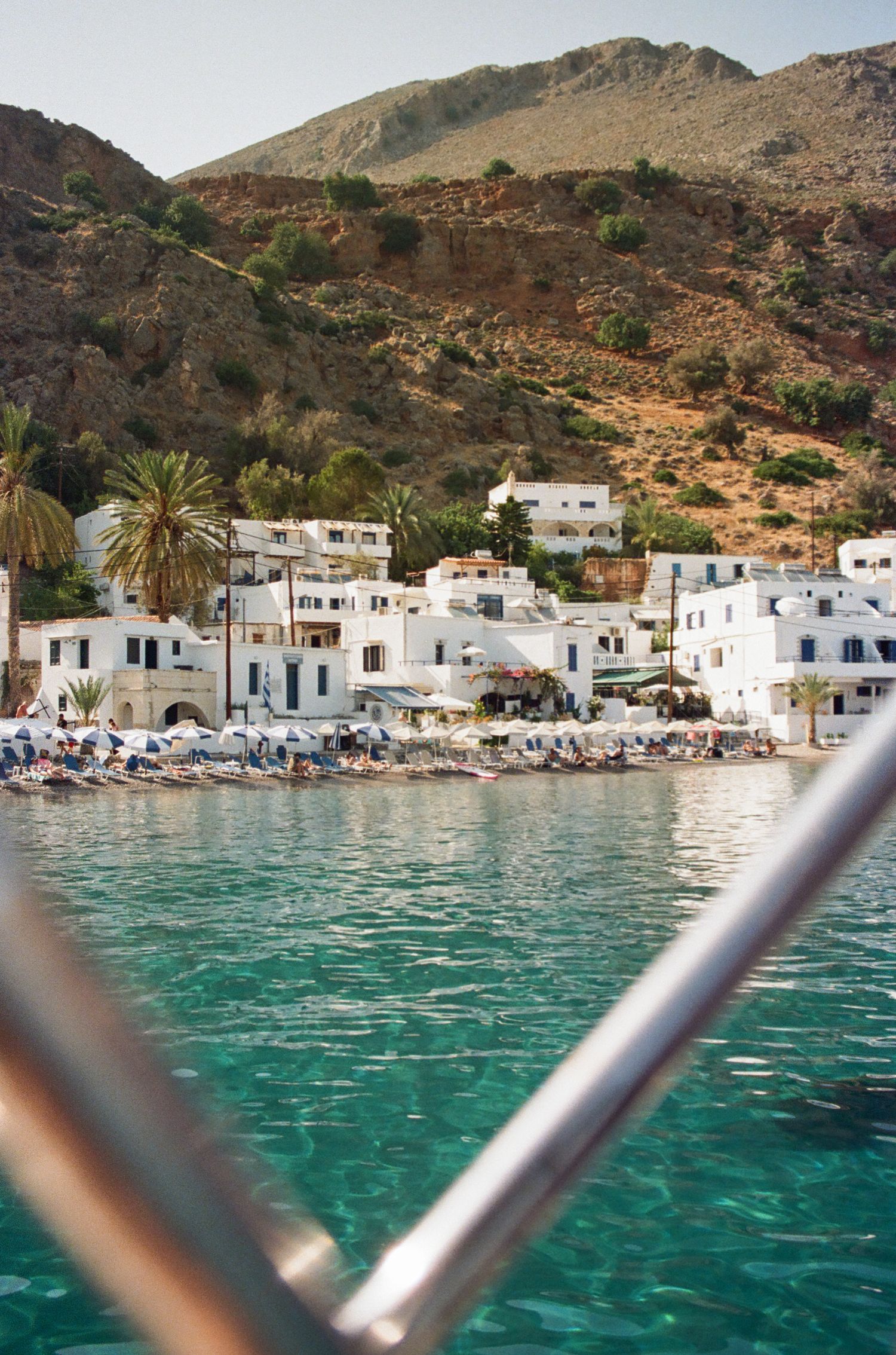 White coastal village with traditional buildings nestled against mountains beside turquoise Mediterranean waters.