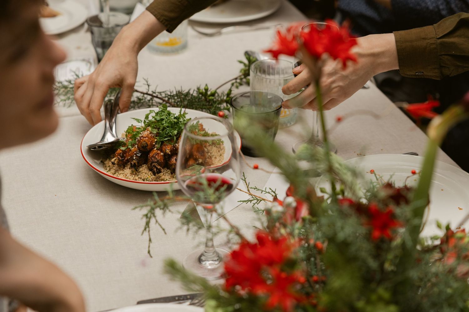 Elegant table setting with fresh flowers and hands serving food at a dinner party.