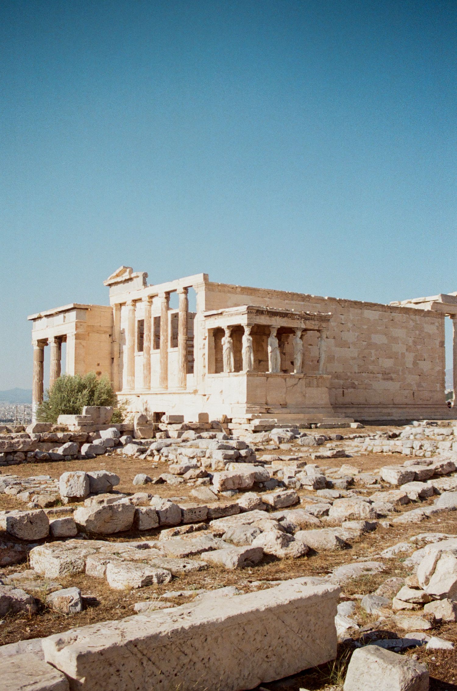 Ancient ruins of the Acropolis with stone columns and architectural remains against blue sky.