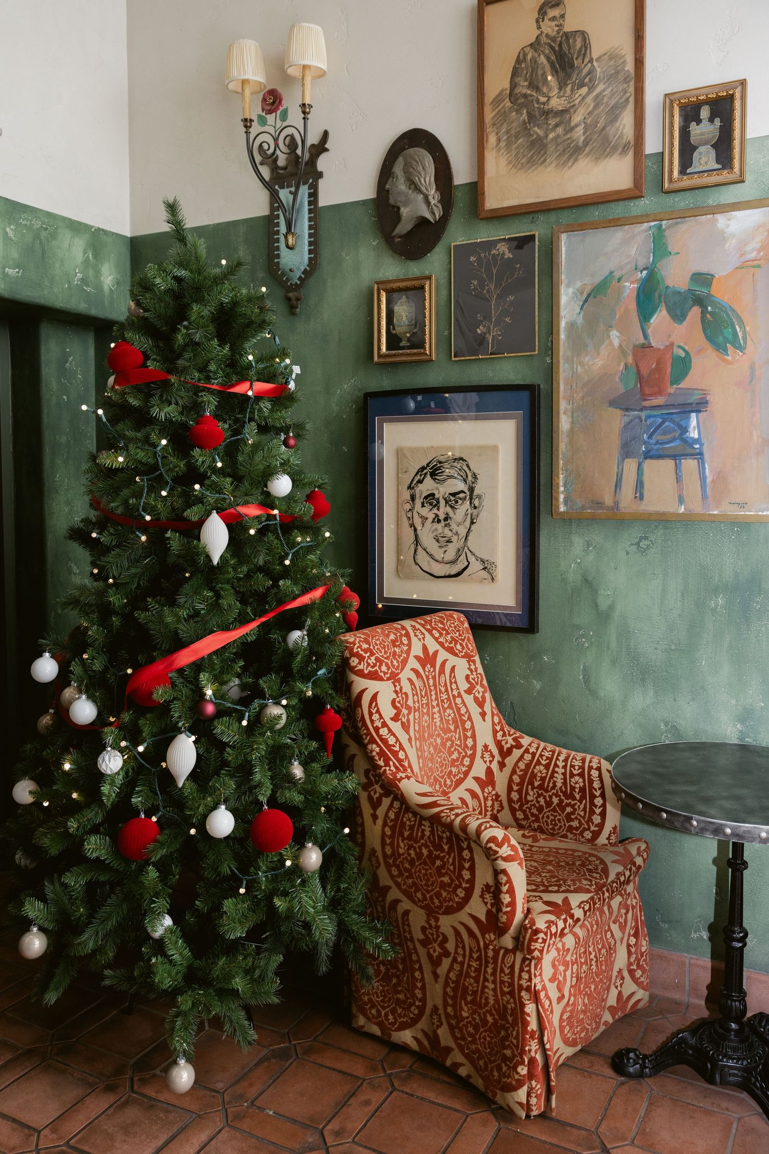 A cozy corner decorated for Christmas with a tree, vintage artwork, and a patterned armchair.