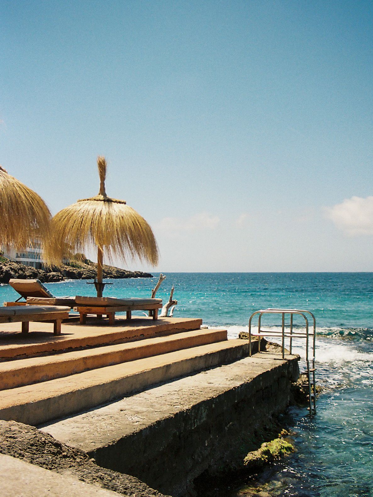 Seaside terrace with thatched umbrellas and lounge chairs overlooking turquoise ocean waters on a sunny day.