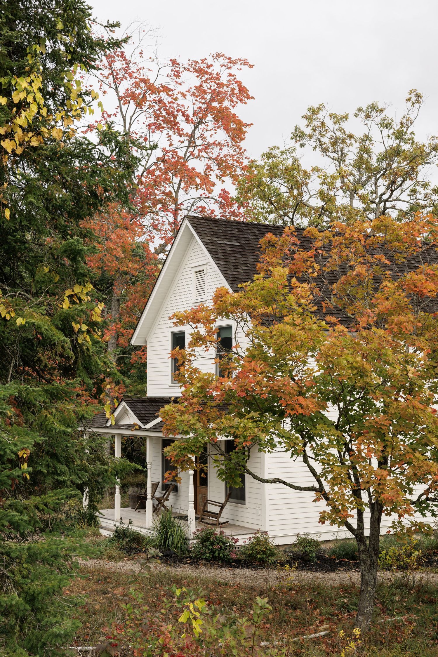 White farmhouse with wrap-around porch nestled among vibrant autumn trees.