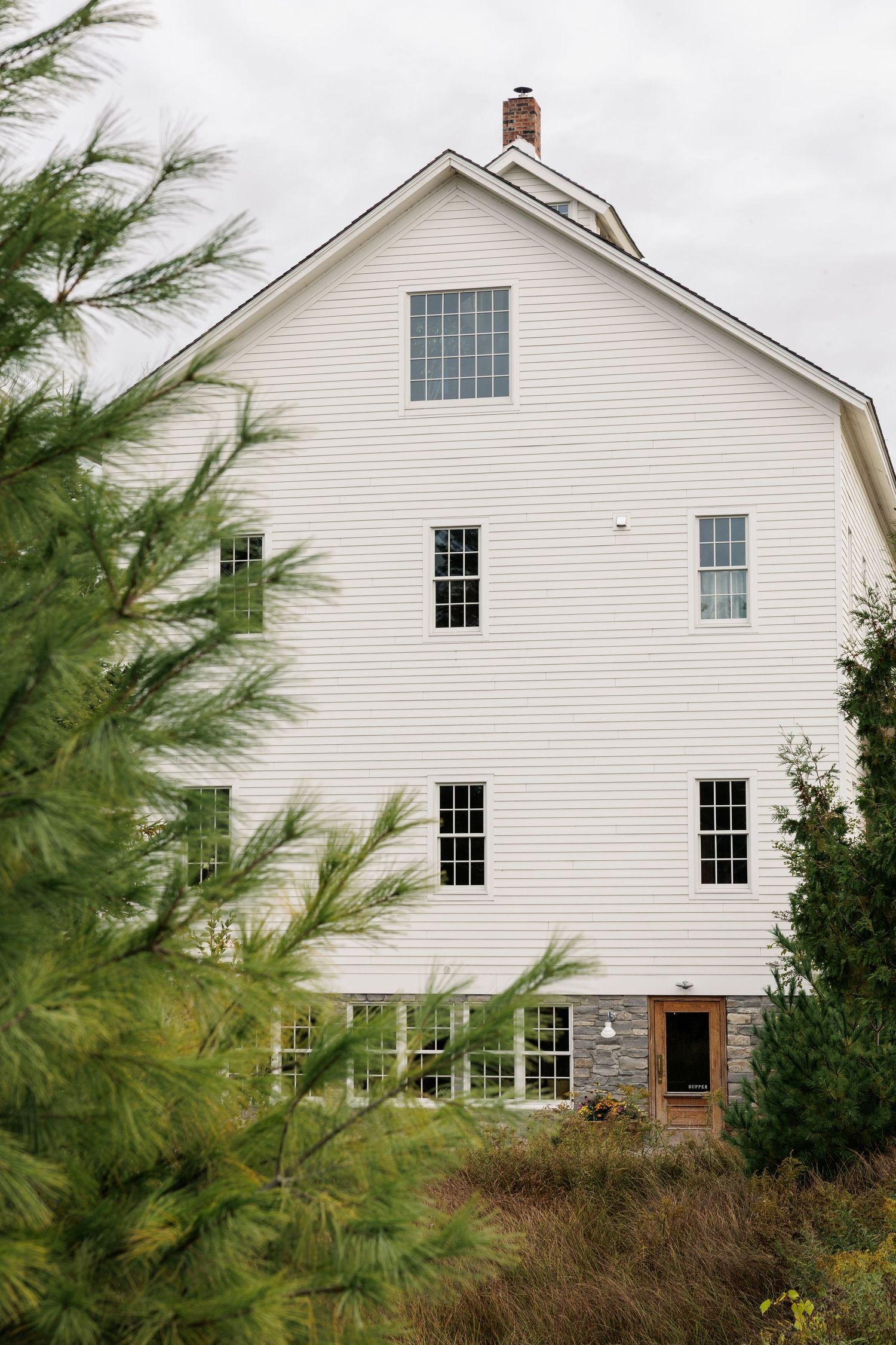 Classic white farmhouse exterior with symmetrical windows and dark trim against an overcast sky.