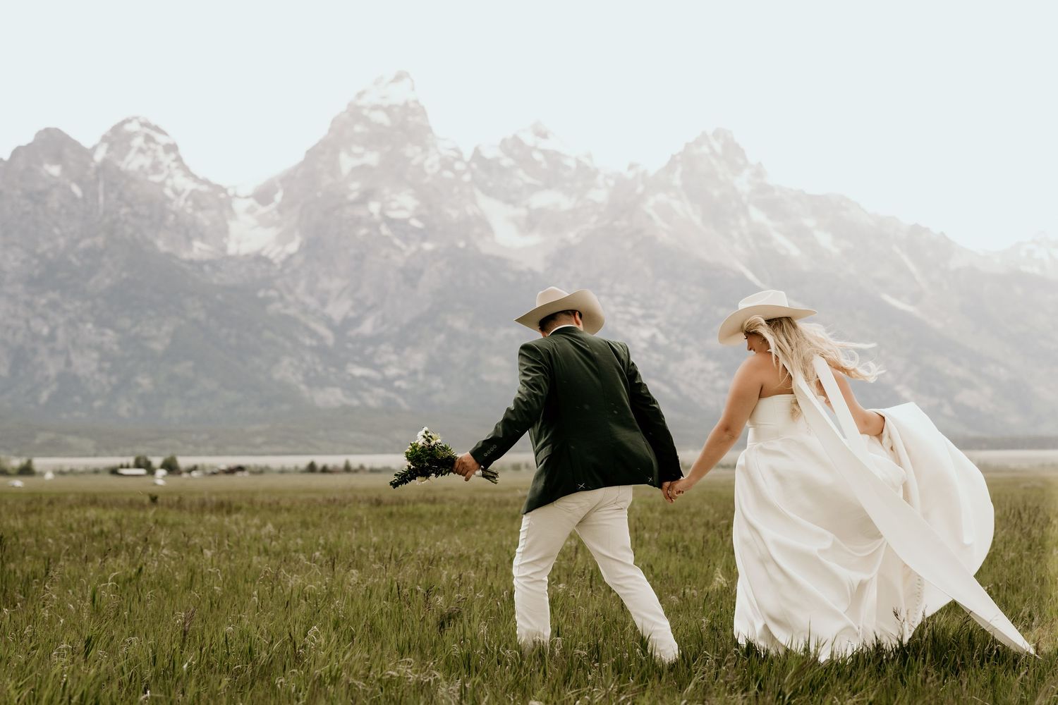 Bride and groom holding hands running through a meadow with the Grand Teton mountains in the background.