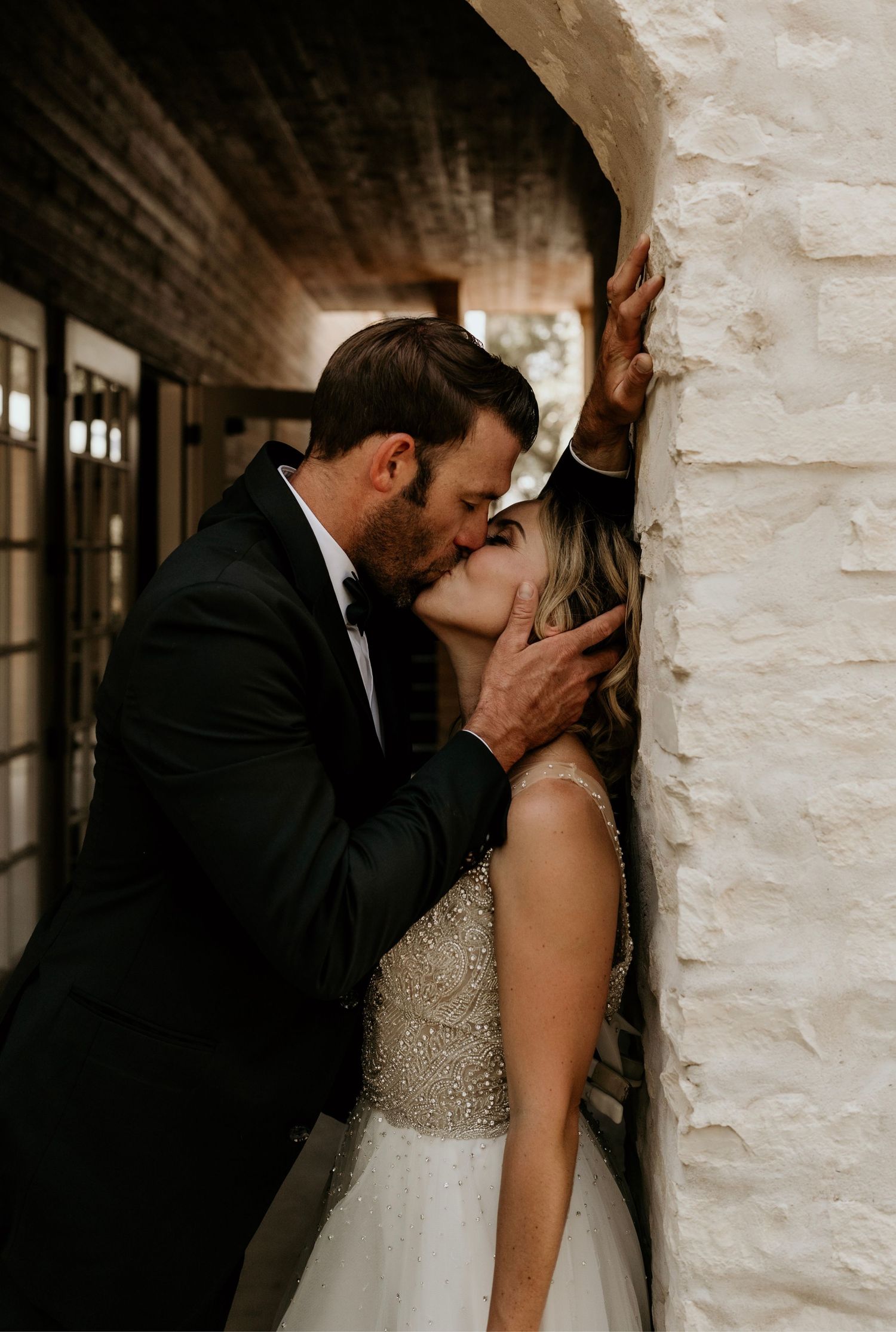 An intimate wedding portrait against a white stone wall with natural lighting.