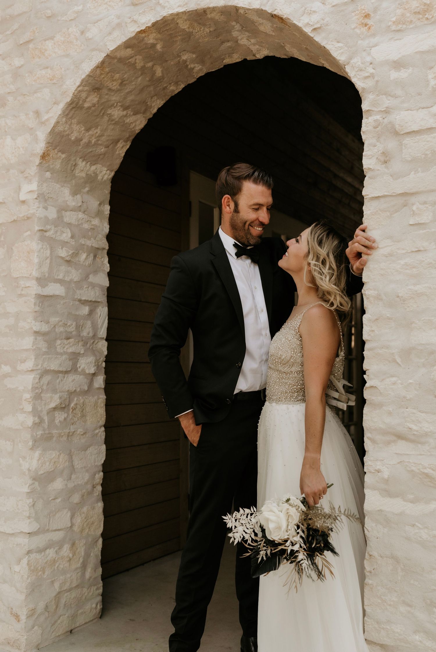Elegant couple sharing an intimate moment under white stone archways.