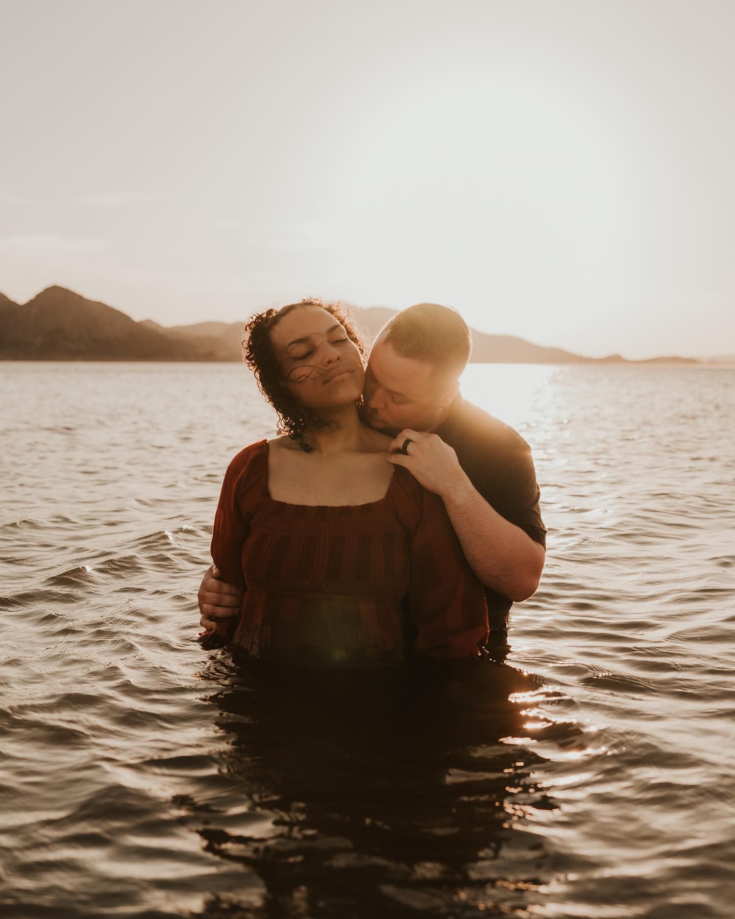 Romantic couple embraces while floating in tranquil water during sunset.