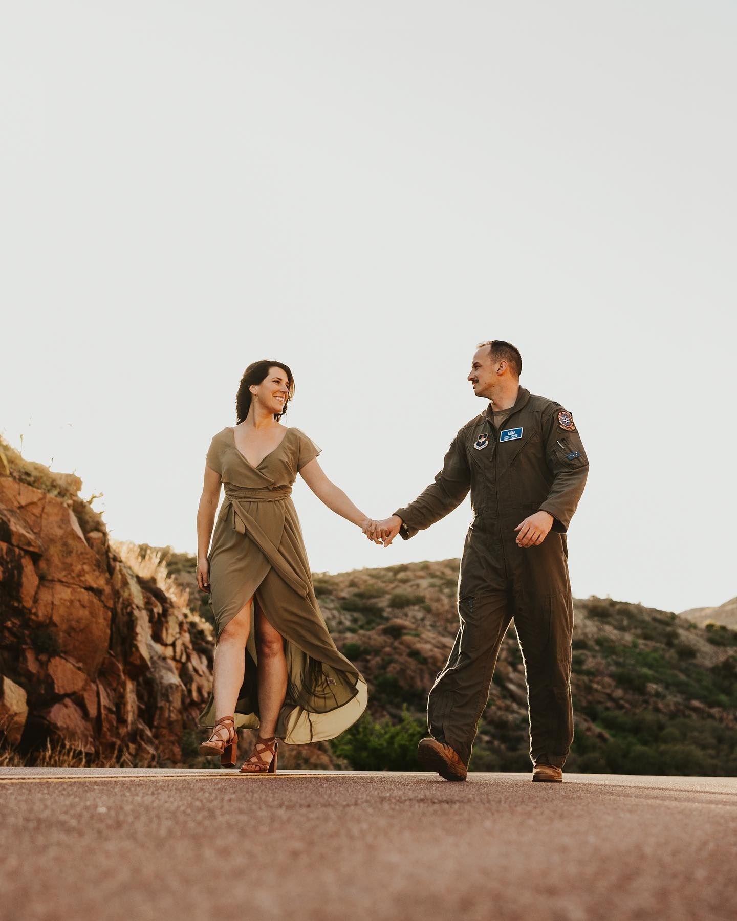 Couple walks hand in hand on a rocky mountain path at sunset.
