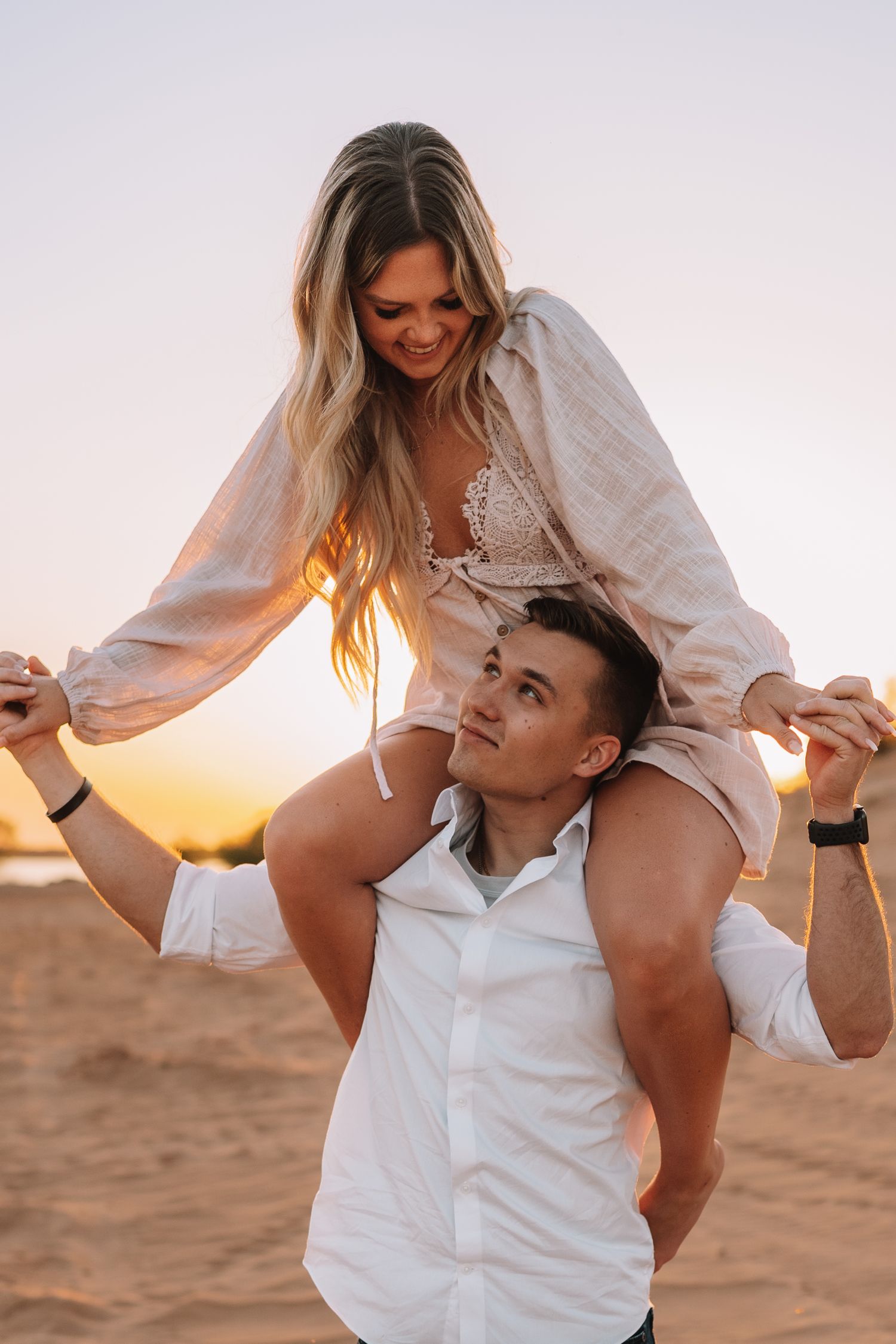 Romantic couple embracing on sandy beach during golden hour sunset photoshoot.