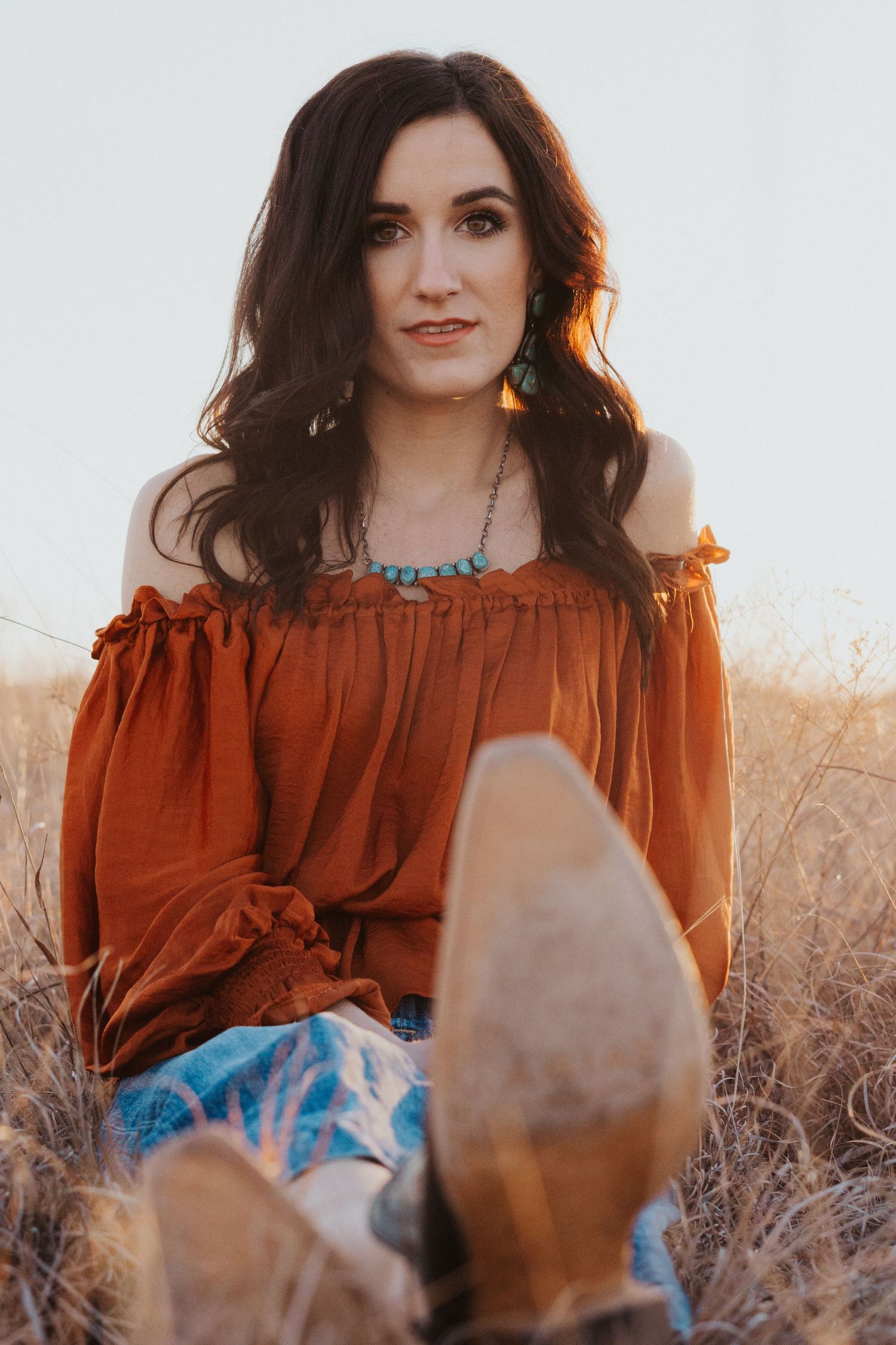 Portrait of a woman in a rust-colored off-shoulder top against a natural backdrop.
