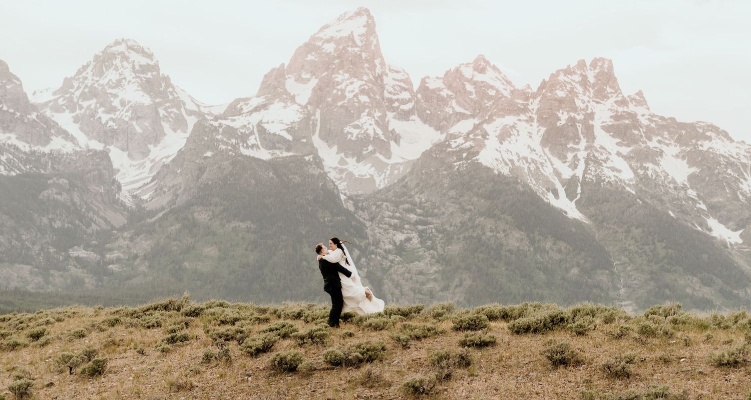 Couple embracing in front of the majestic Grand Teton mountain range during their outdoor wedding ceremony.